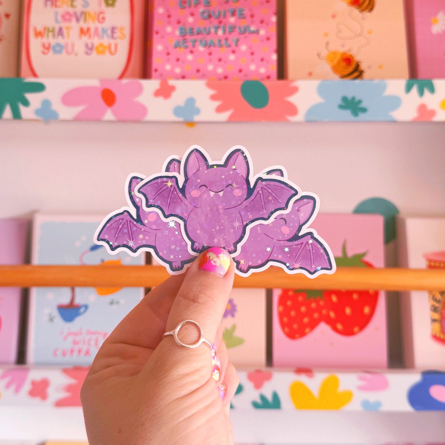 A holographic halloween themed sticker featuring an illustration of a purple bat with a navy border.