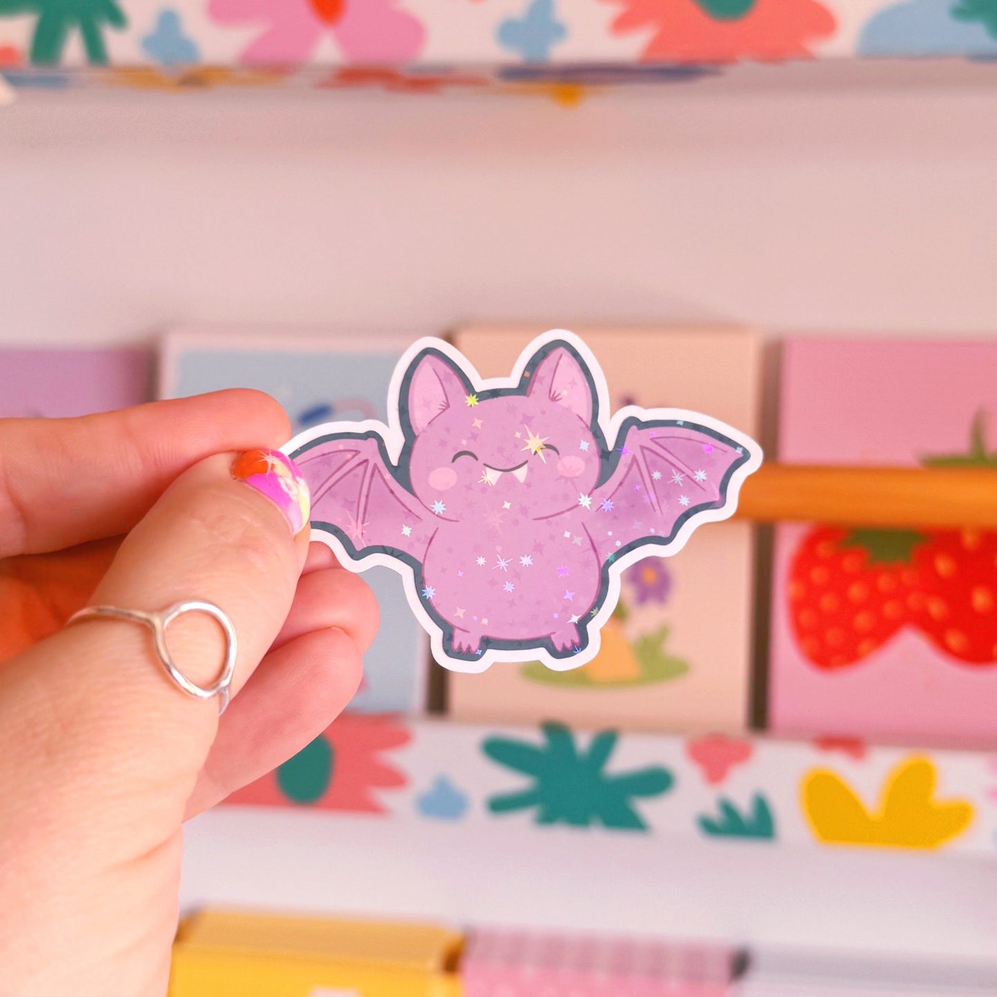 A holographic halloween themed sticker featuring an illustration of a purple bat with a navy border.