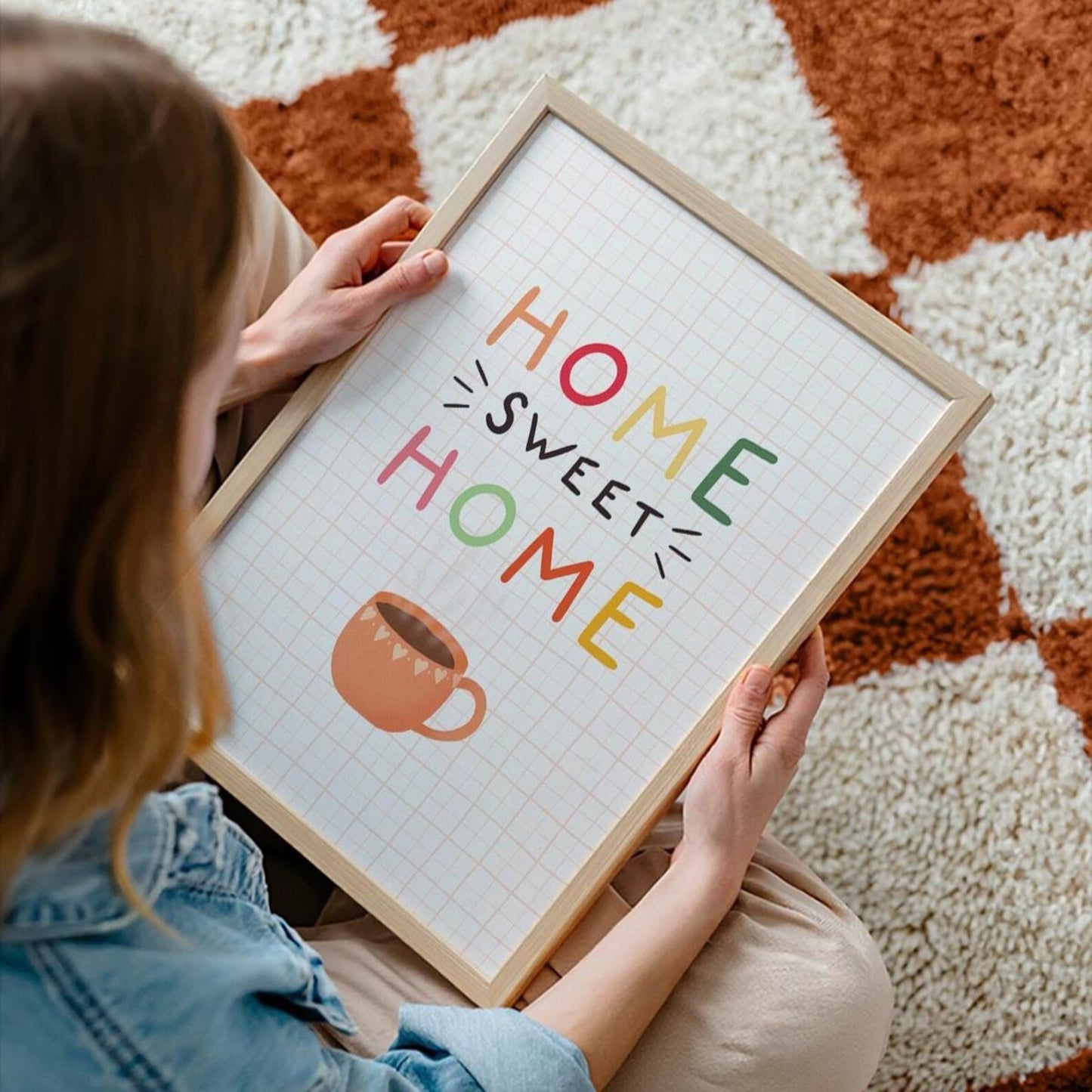A cosy quote print that reads 'home sweet home' with an orange mug of coffee underneath. The background of the print is cream with a soft orange checkered pattern.