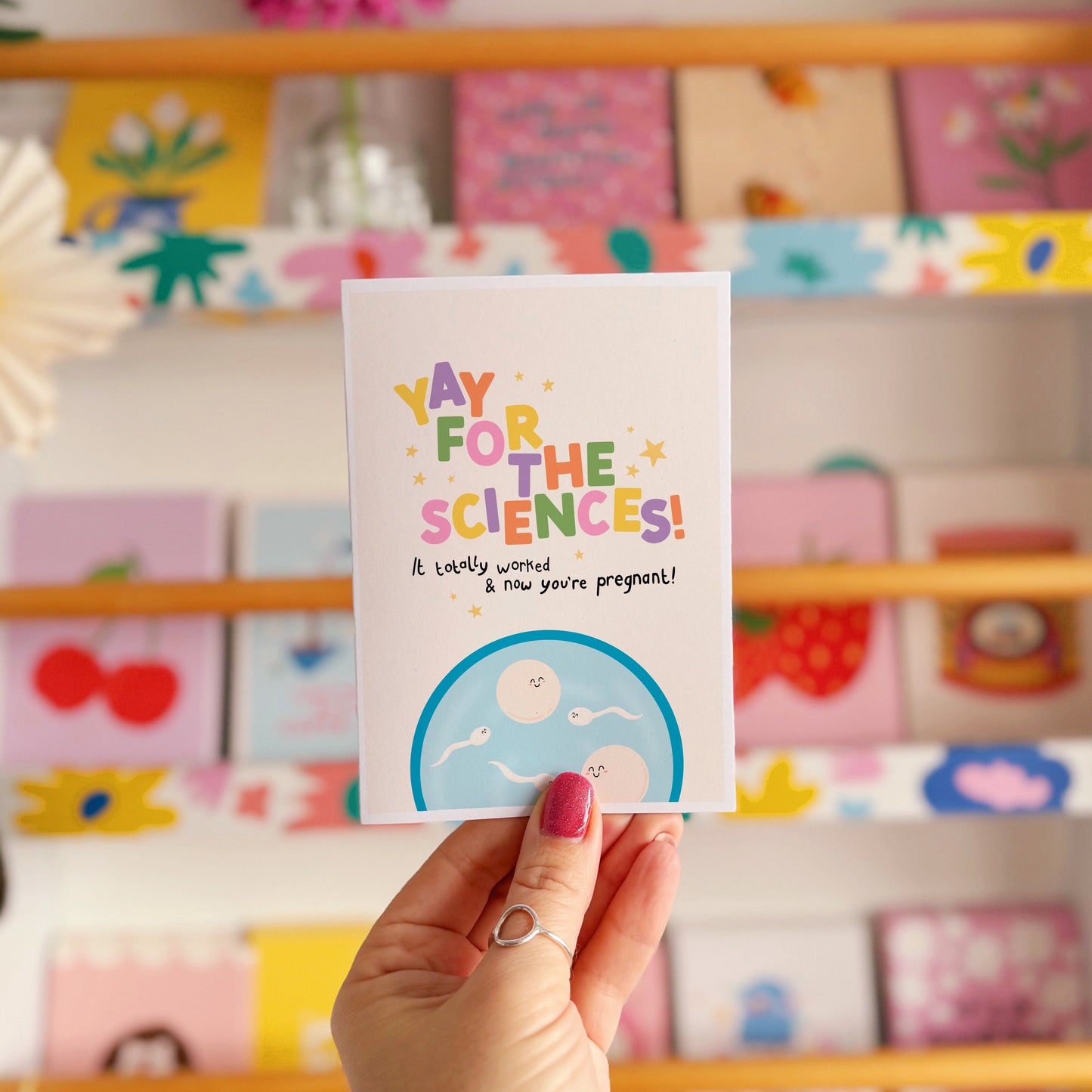 A congratulations card for pregnancy via IVF, with colourful lettering and a little illustration of a petri dish with cartoon eggs and sperm in.