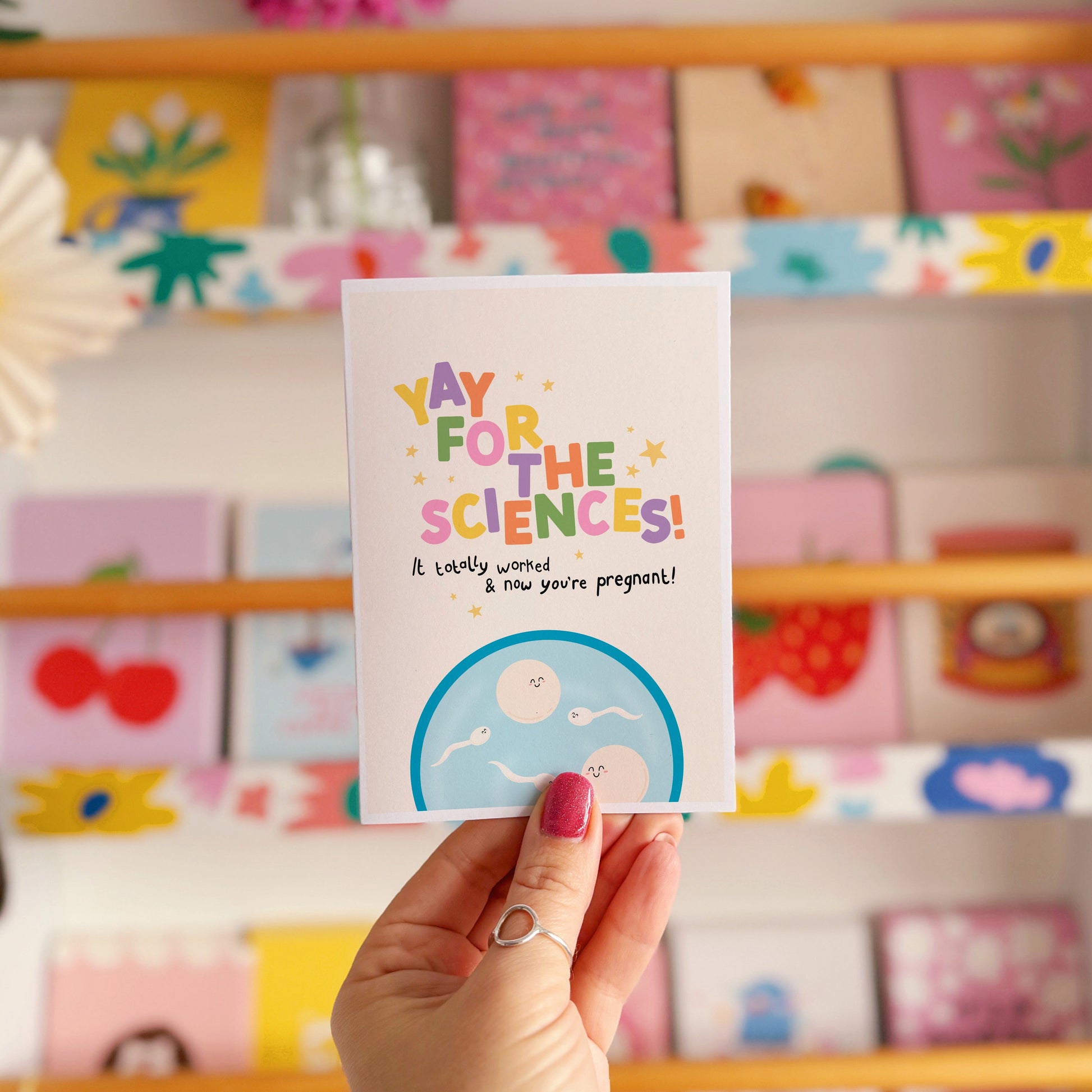 A congratulations card for pregnancy via IVF, with colourful lettering and a little illustration of a petri dish with cartoon eggs and sperm in.
