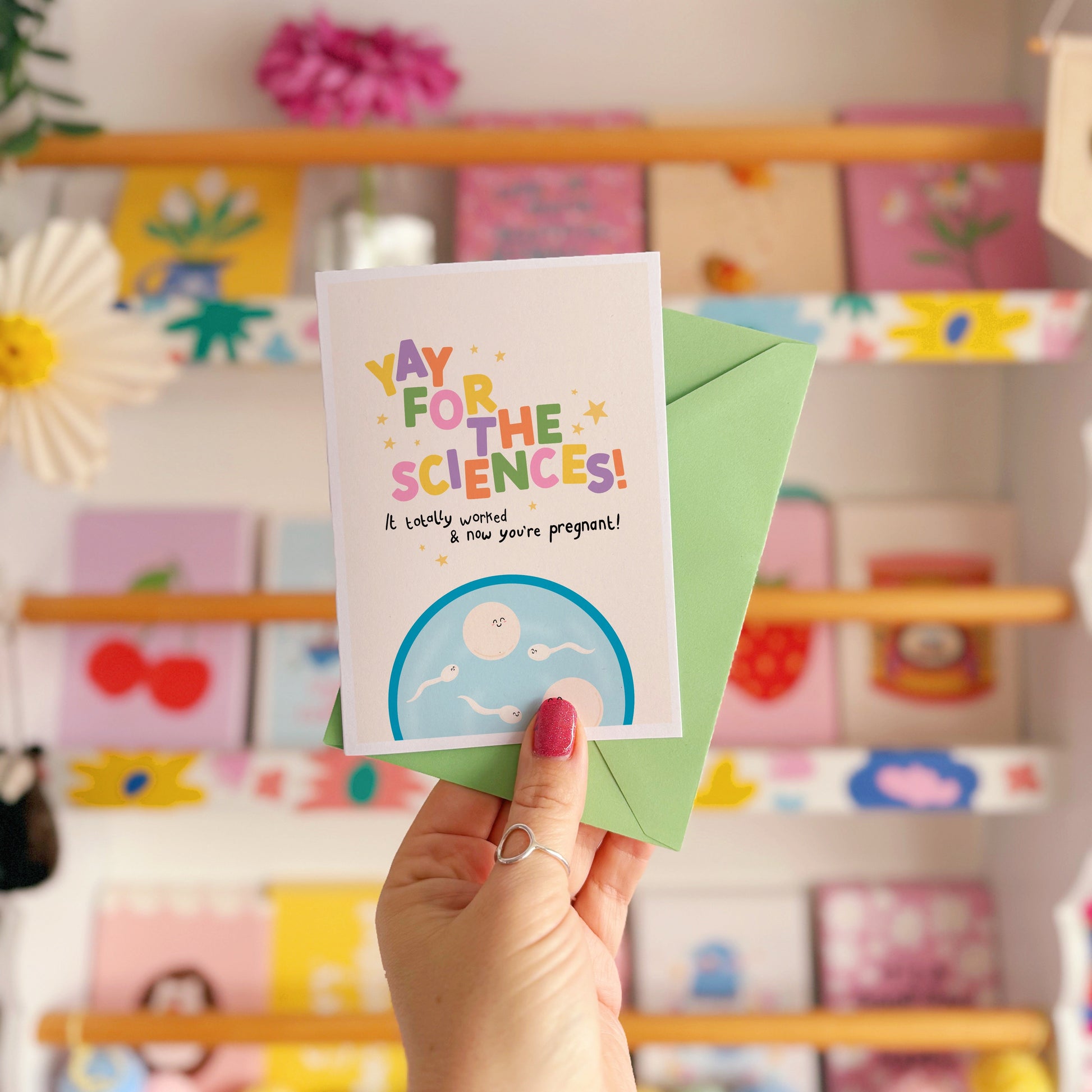 A congratulations card for pregnancy via IVF, with colourful lettering and a little illustration of a petri dish with cartoon eggs and sperm in.