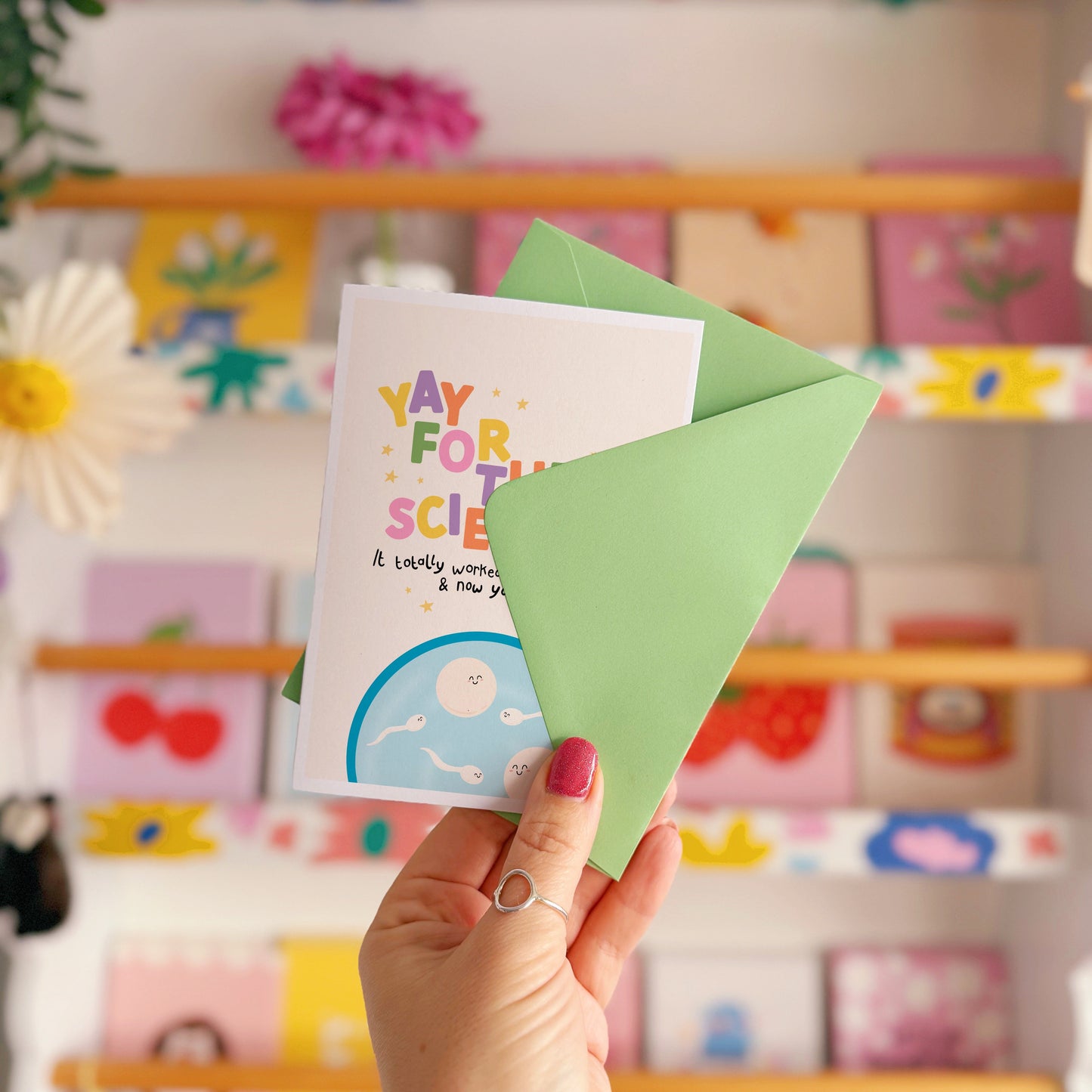 A congratulations card for pregnancy via IVF, with colourful lettering and a little illustration of a petri dish with cartoon eggs and sperm in.