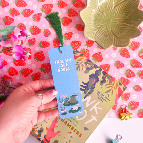 A blue bookmark with a cute frog illustration to both the front and back of the bookmark, on the front of the bookmark it says 'I Froggin' Love Books' and on the back of the bookmark is the brand logo.