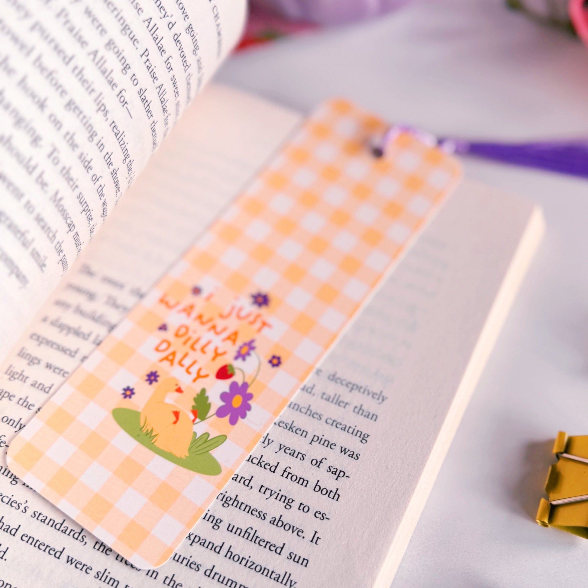 A yellow gingham bookmark with an illustration of a little duck with purple flowers. The text on the bookmark reads 'I just wanna dilly dally'.