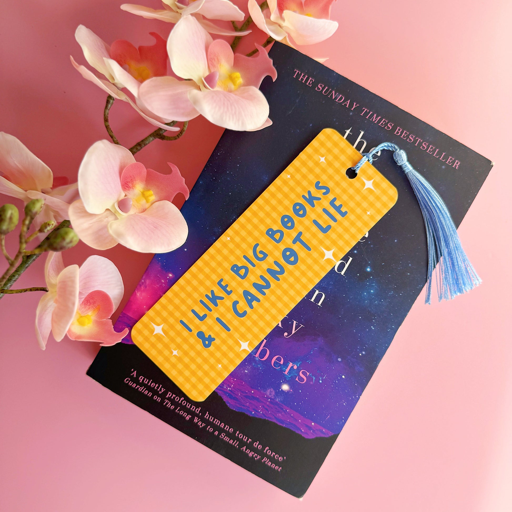 A yellow gingham bookmark, with a blue tassel, and blue text that reads 'I like big books and I cannot lie'.