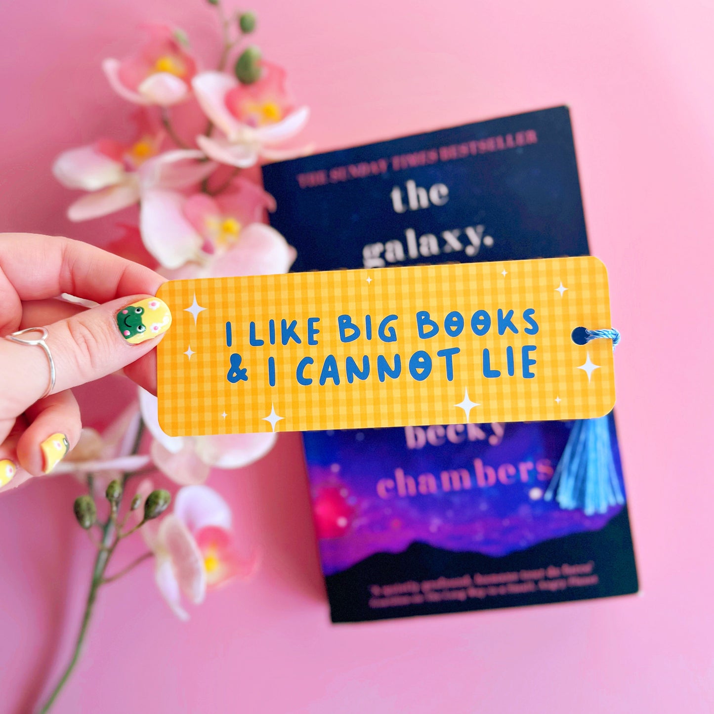 A yellow gingham bookmark, with a blue tassel, and blue text that reads 'I like big books and I cannot lie'.