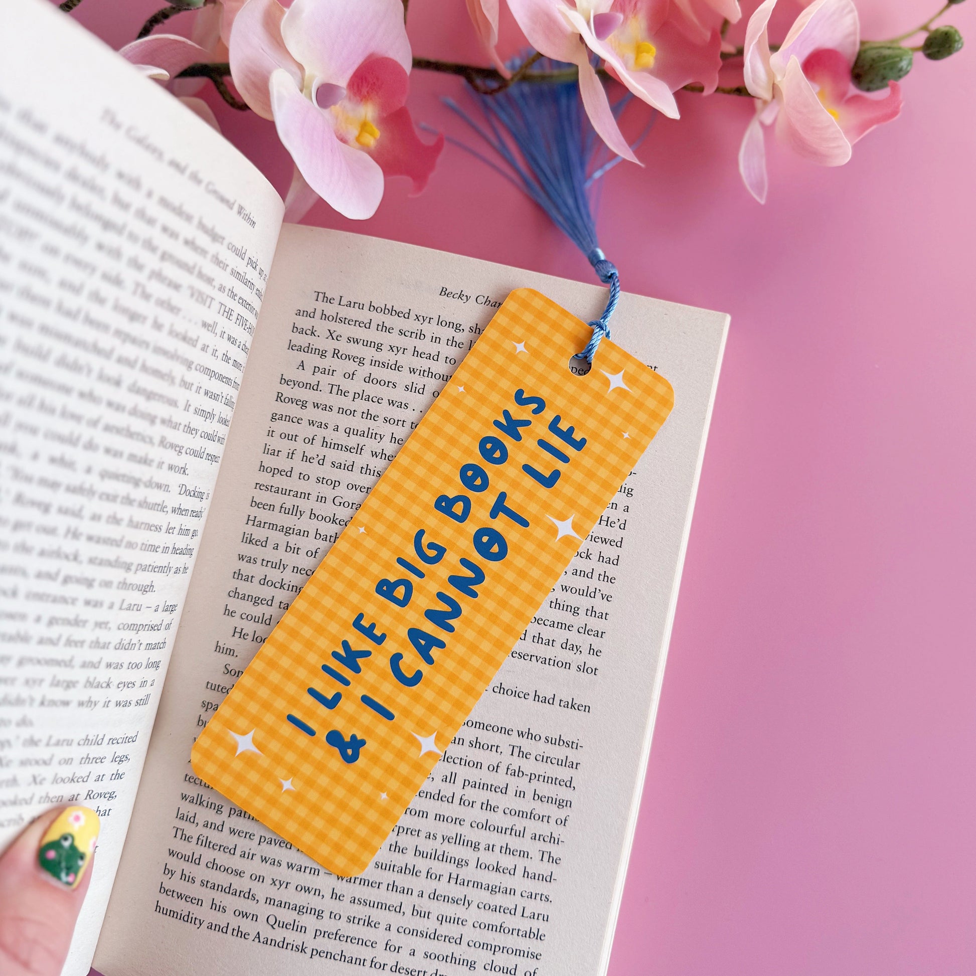 A yellow gingham bookmark, with a blue tassel, and blue text that reads 'I like big books and I cannot lie'.