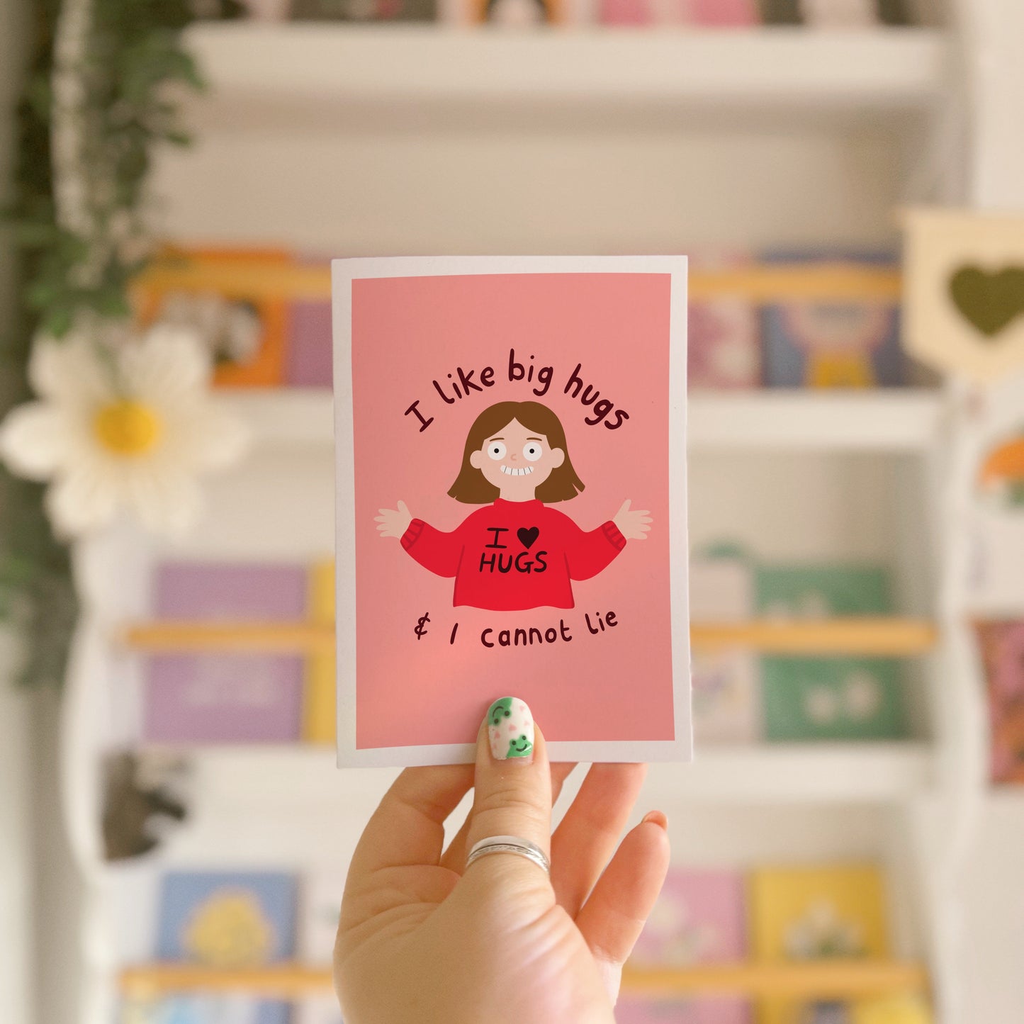 A pinkish red card with an illustration of a slightly creepy looking woman wearing a red jumper that says 'I love hugs' and text around her saying 'I like big hugs and I cannot lie'.