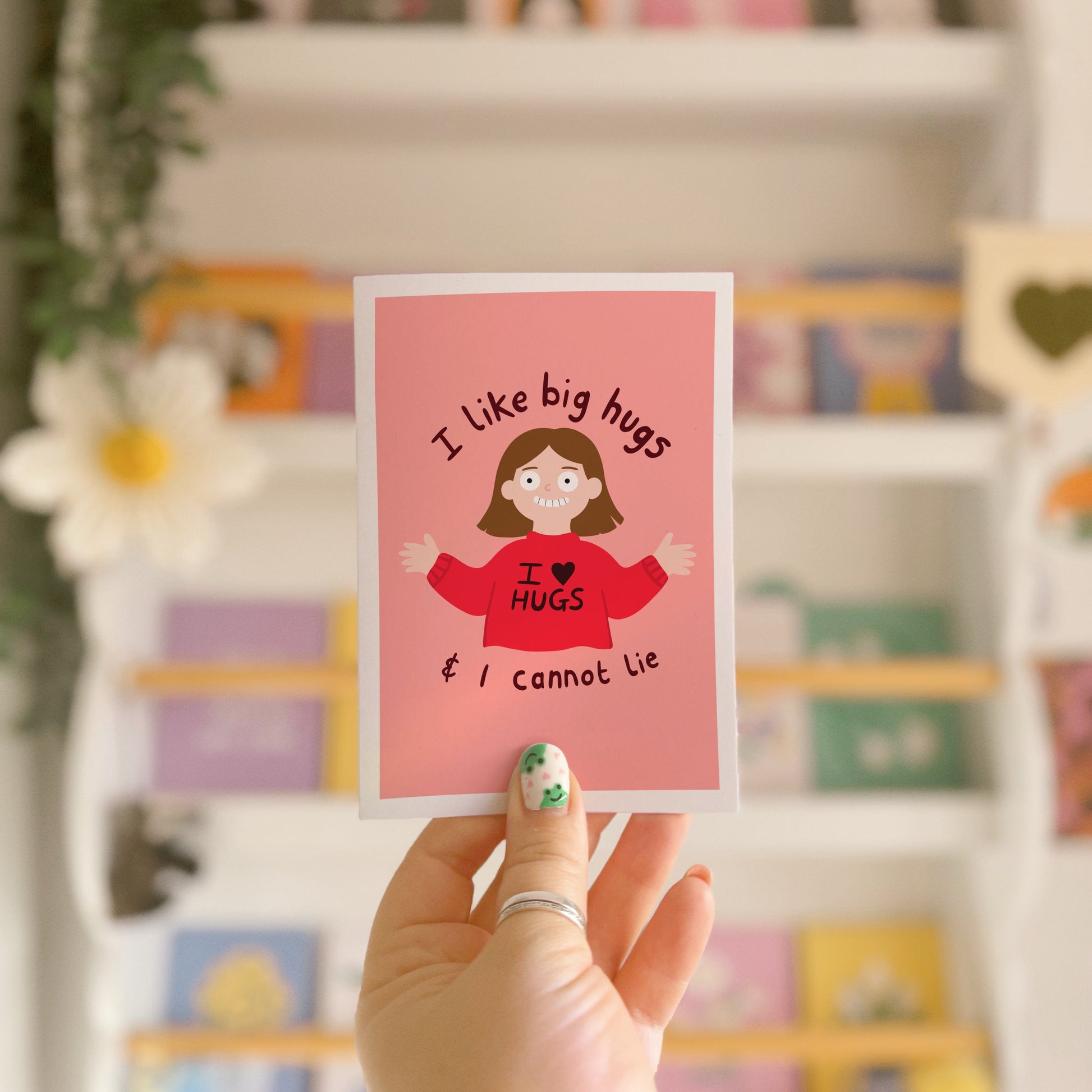 A pinkish red card with an illustration of a slightly creepy looking woman wearing a red jumper that says 'I love hugs' and text around her saying 'I like big hugs and I cannot lie'.