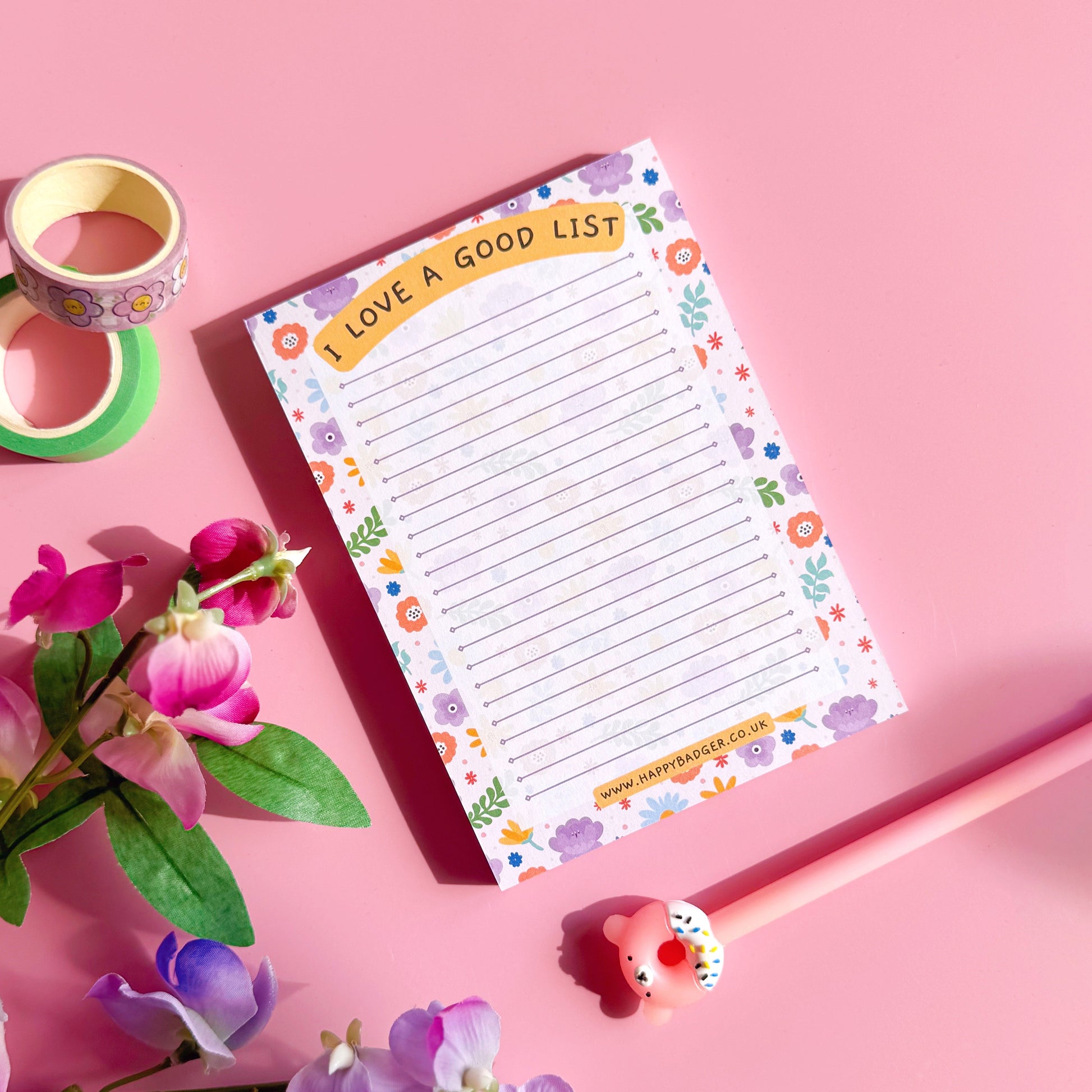Notebook with floral design on a pink background with flowers and tape.