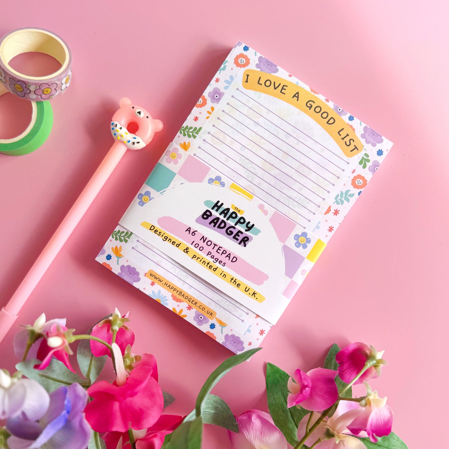 Notepad with floral design on a pink background with flowers and tape.