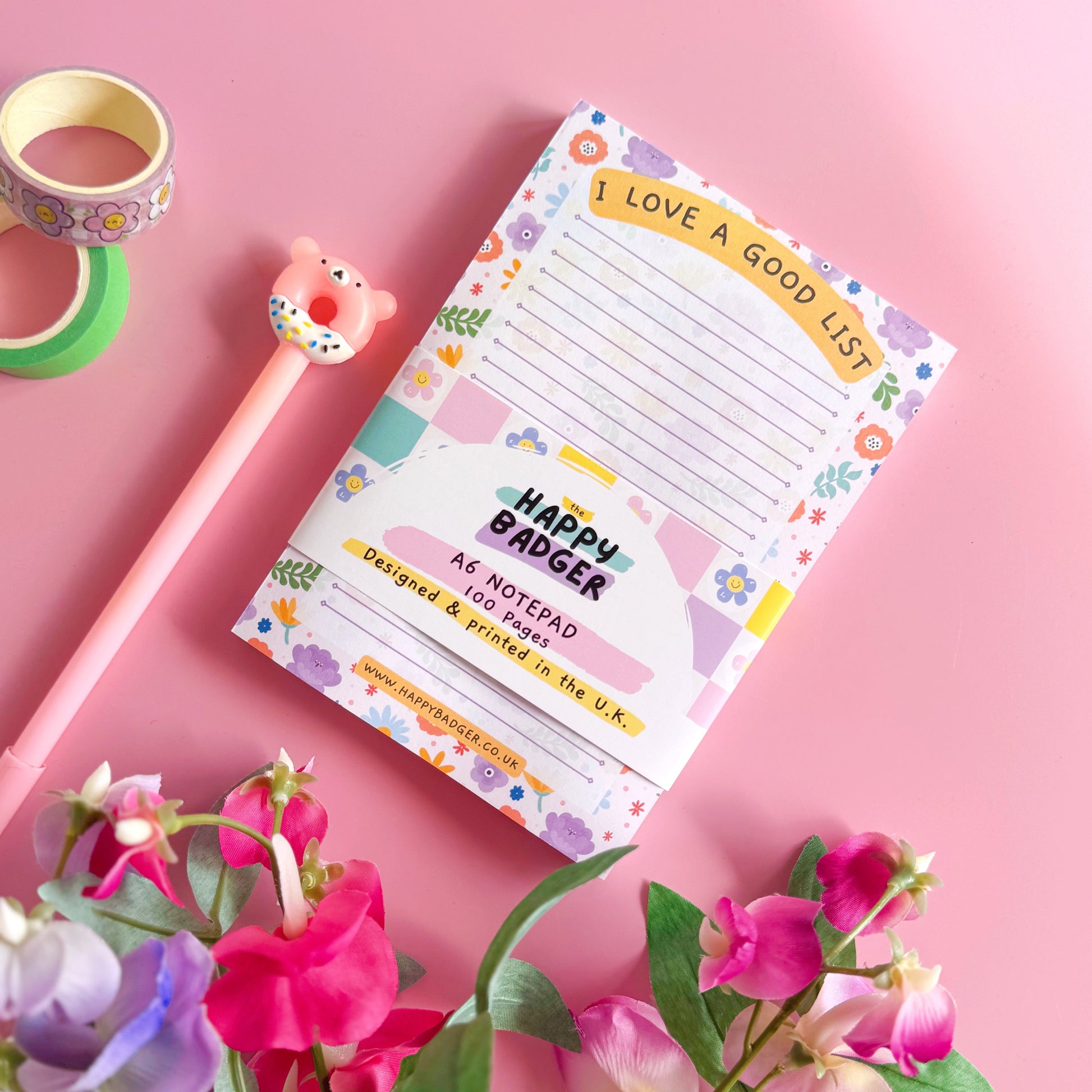 Notepad with floral design on a pink background with flowers and tape.