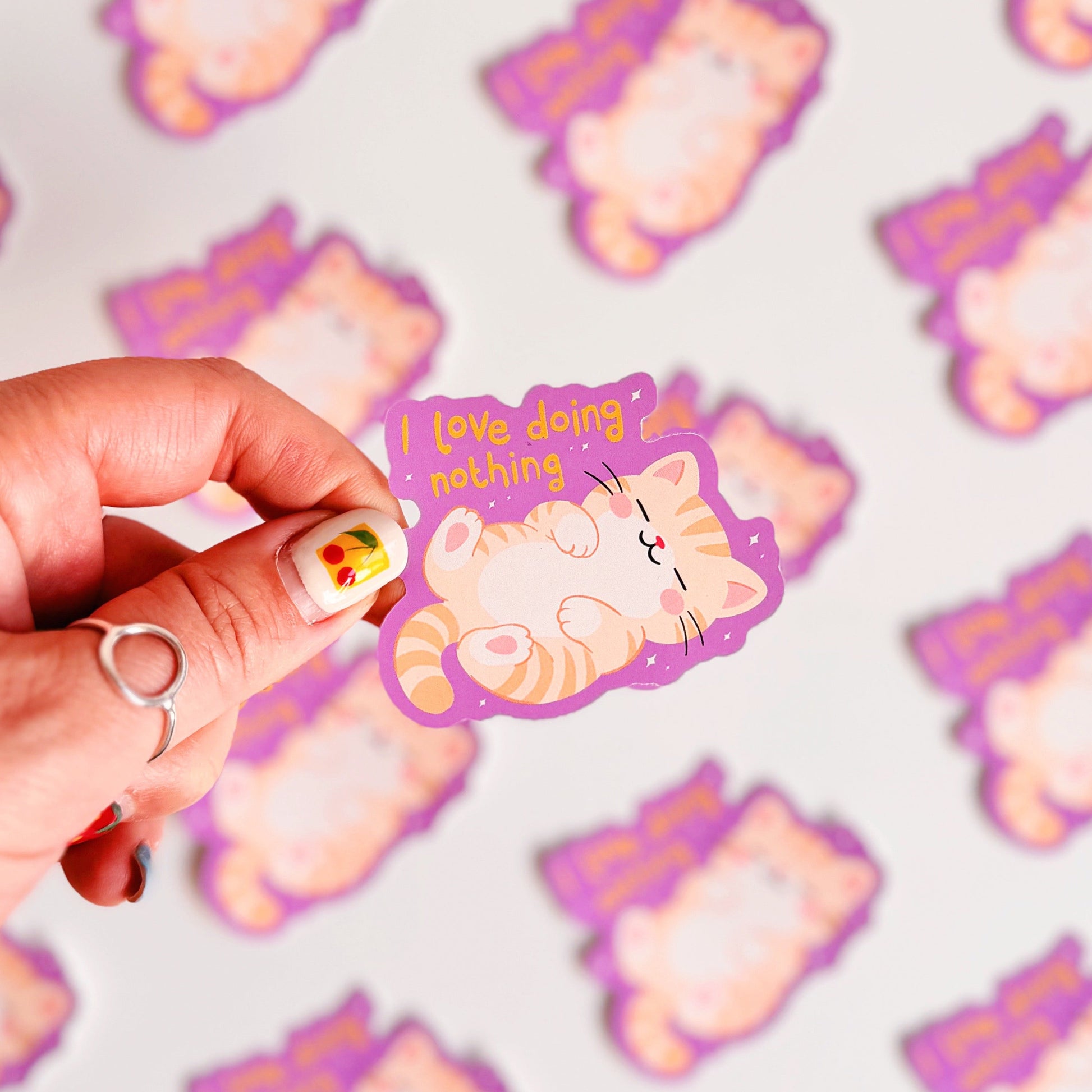 A purple vinyl sticker with an illustration of a sleeping cat, next to a hand lettered quote that reads 'I love doing nothing'.