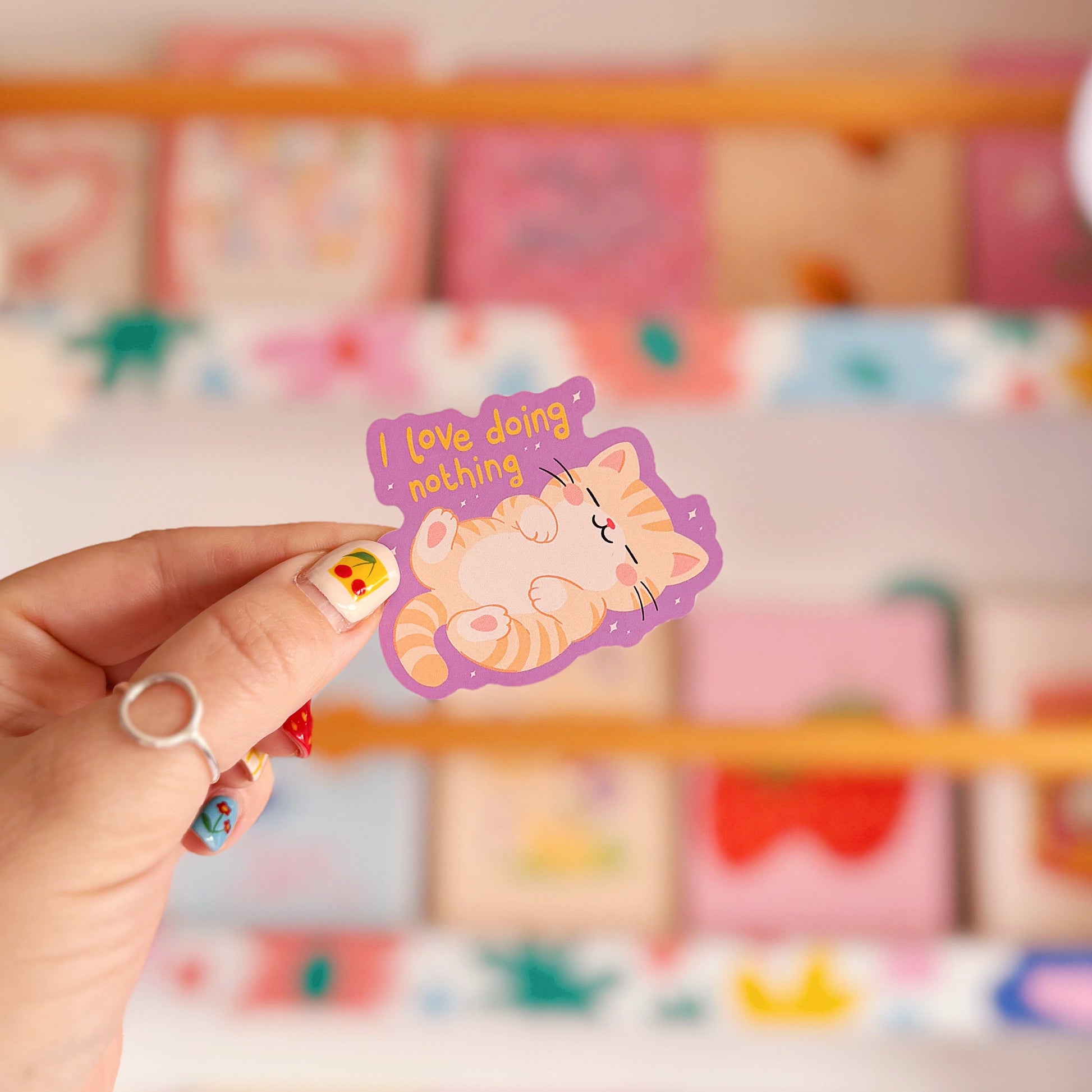 A purple vinyl sticker with an illustration of a sleeping cat, next to a hand lettered quote that reads 'I love doing nothing'.
