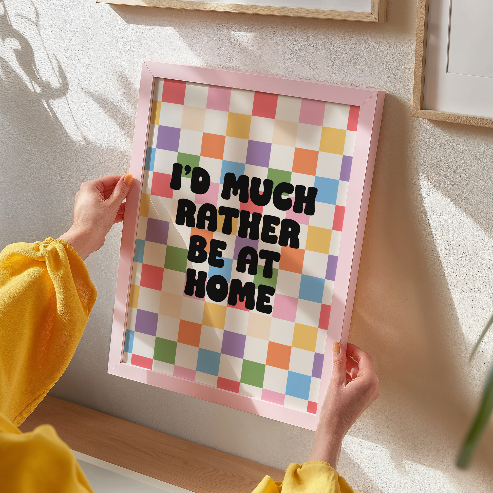 A colourful checkered print with the text 'I'd much rather be at home' centred, set against a white background.
