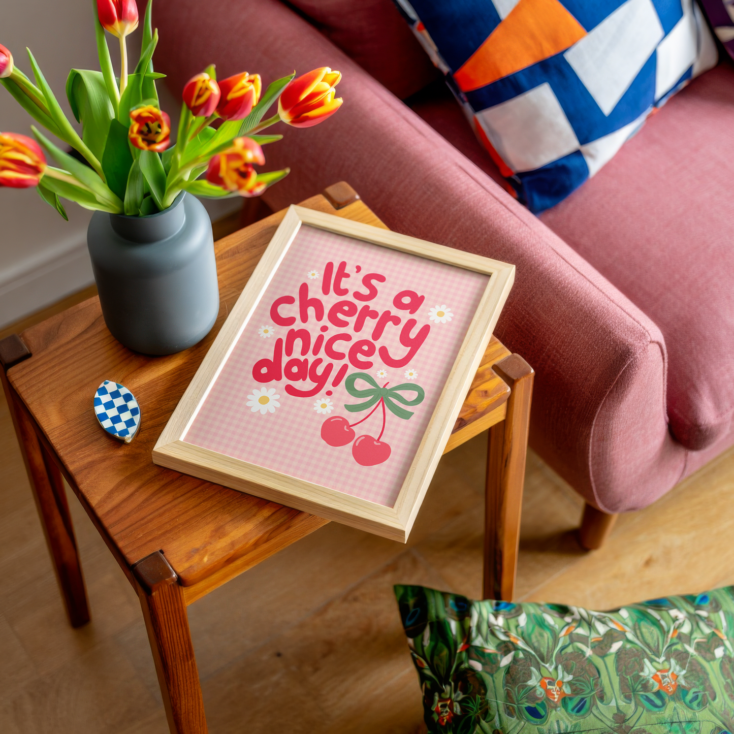 A gingham print, with hand lettered text that reads 'it's a cherry nice day!' in red. The text is surrounded by little daisy illustrations and a large pair of cherries tied together with a green bow.