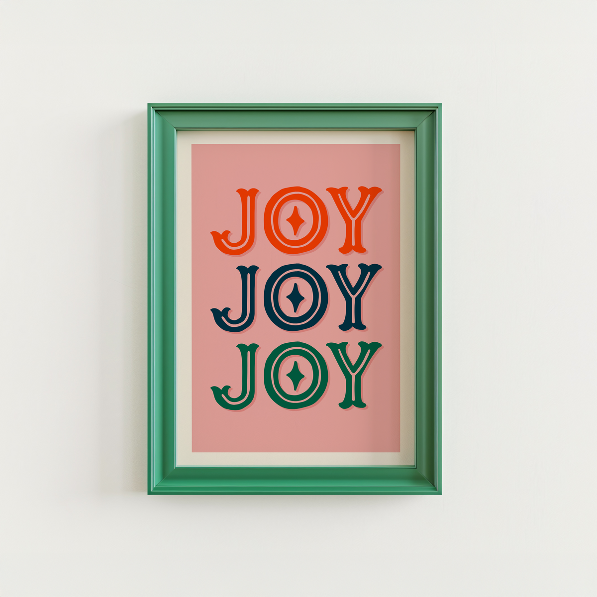 A print with a warm pink background and the word 'joy' written, in an ornate text, three times - one in red, one in navy and one in green.