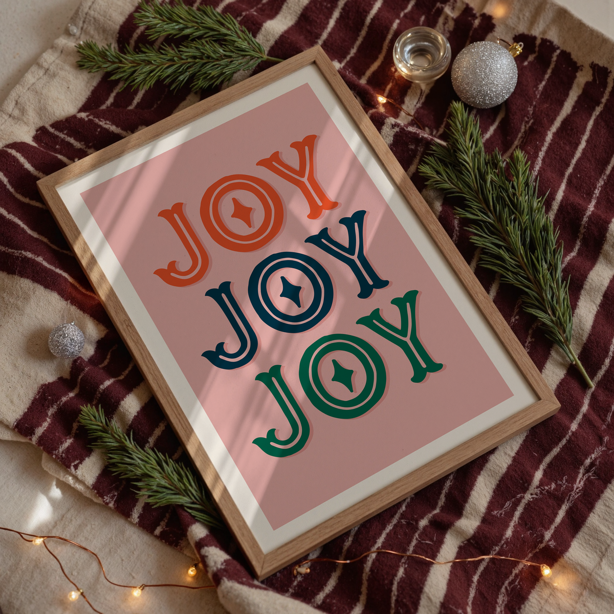 A print with a warm pink background and the word 'joy' written, in an ornate text, three times - one in red, one in navy and one in green.
