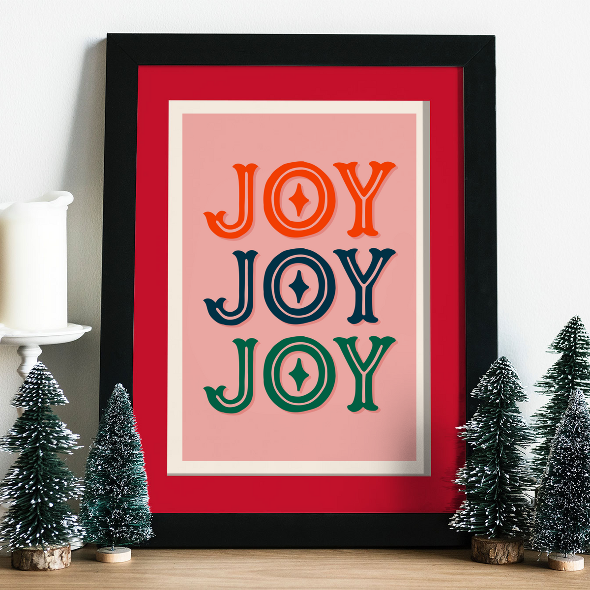 A print with a warm pink background and the word 'joy' written, in an ornate text, three times - one in red, one in navy and one in green.