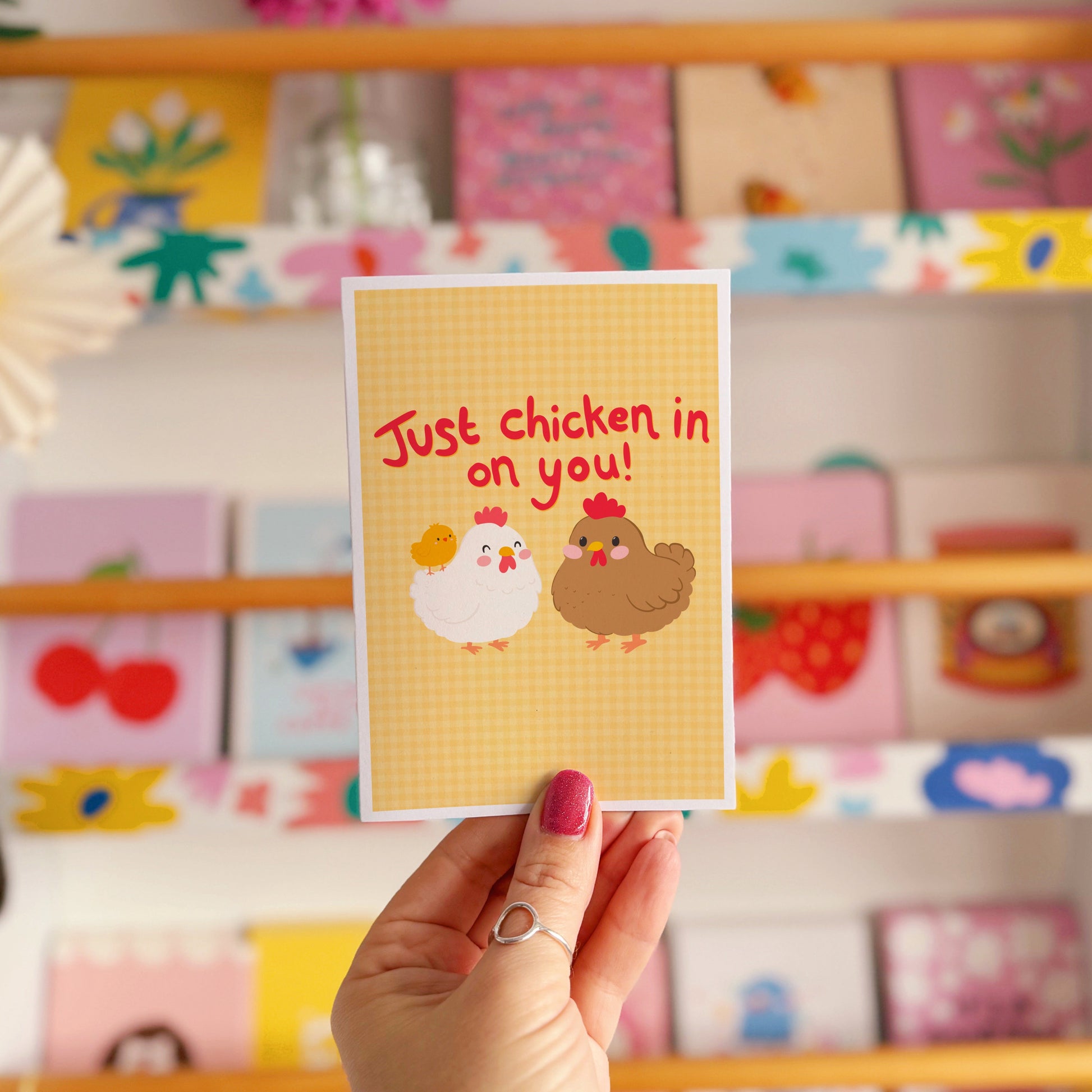 Card with chicken illustrations and red text that says 'Just chicken in on you!', with a yellow gingham background.