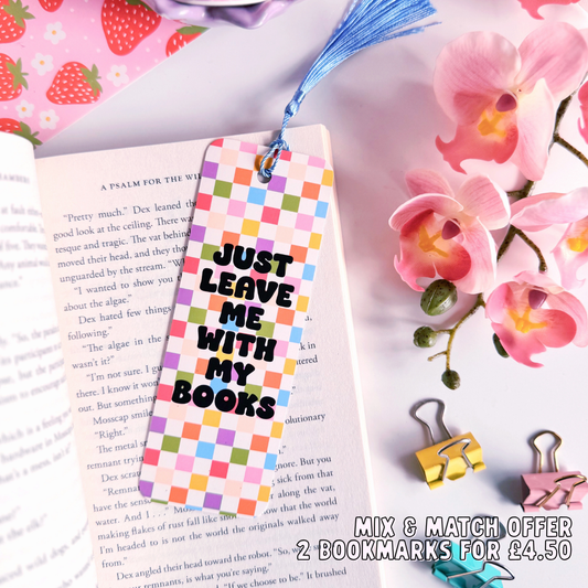 A checkerboard bookmark with rounded corners and a blue tassel, with the words 'just leave me with my books' in bold black writing on the front, and a branding logo on the back.
