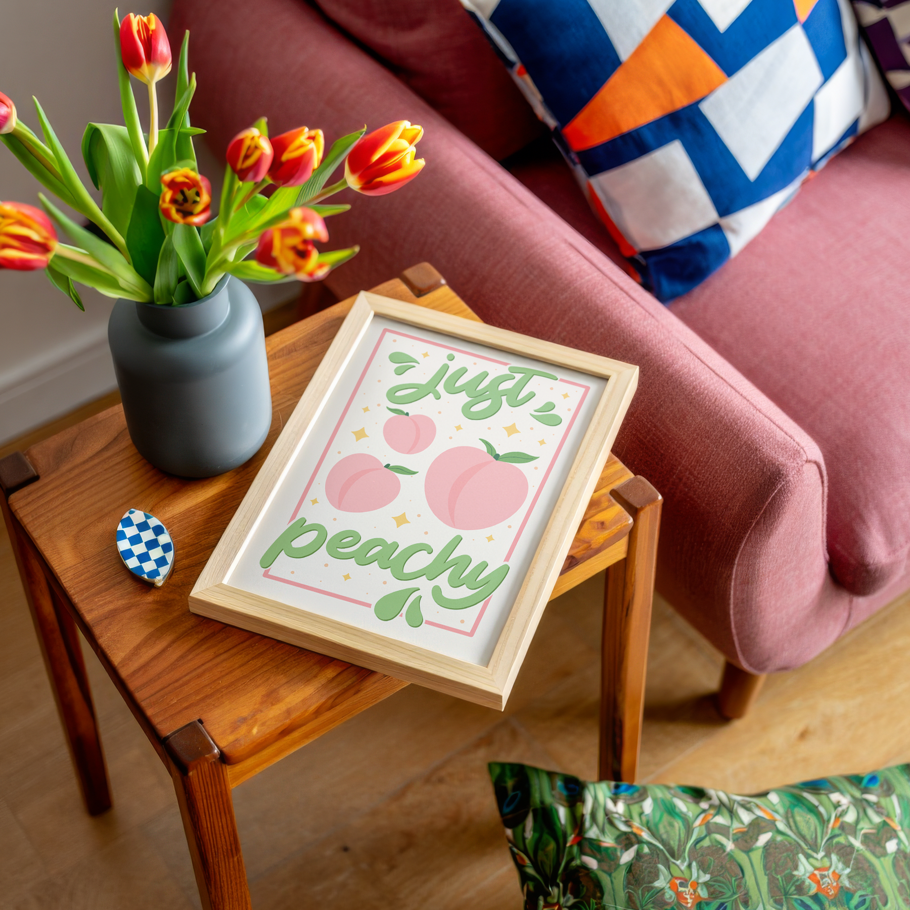 An art print with the text 'just peachy' hand-lettered in teal script, accompanied by illustrations of pink peaches and leaves, and a soft pink border.