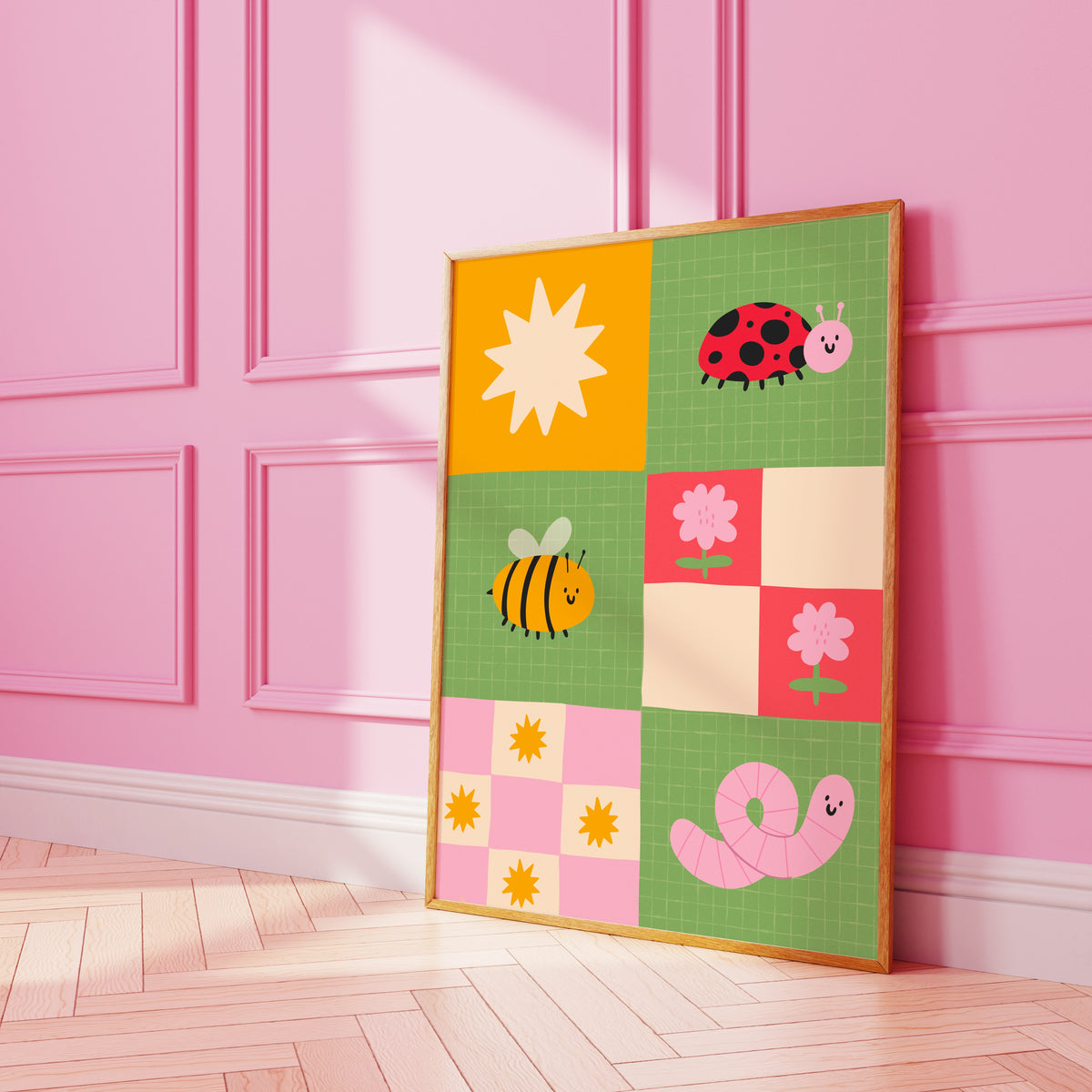 A framed children's art print. The illustration features colourful cartoon motifs including a ladybug, bee, worm, flowers, and suns on green, pink, yellow, and cream squares.