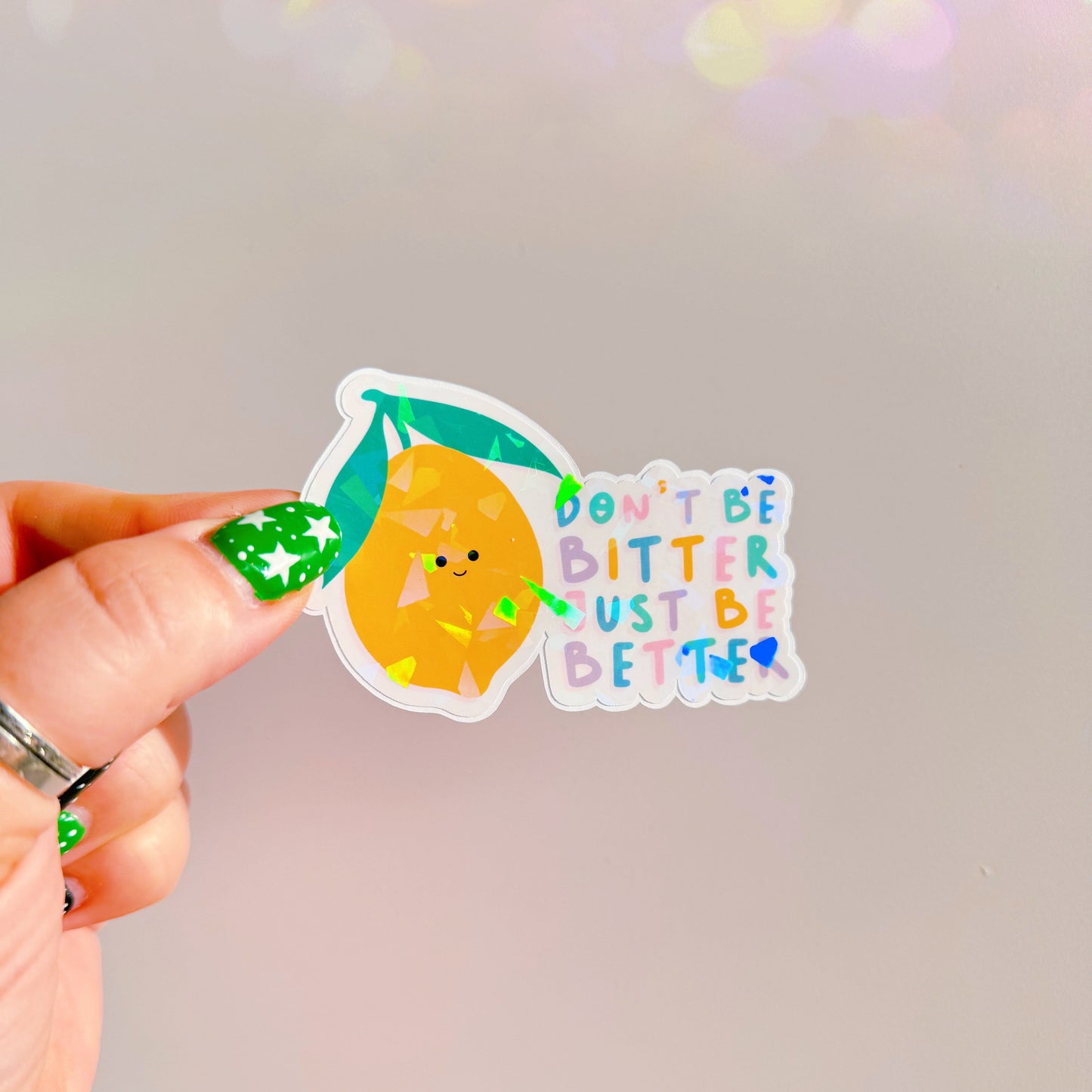 A holographic sticker, of a smiling lemon and the quote don't be bitter just be better. The sticker has an easy peel lip.