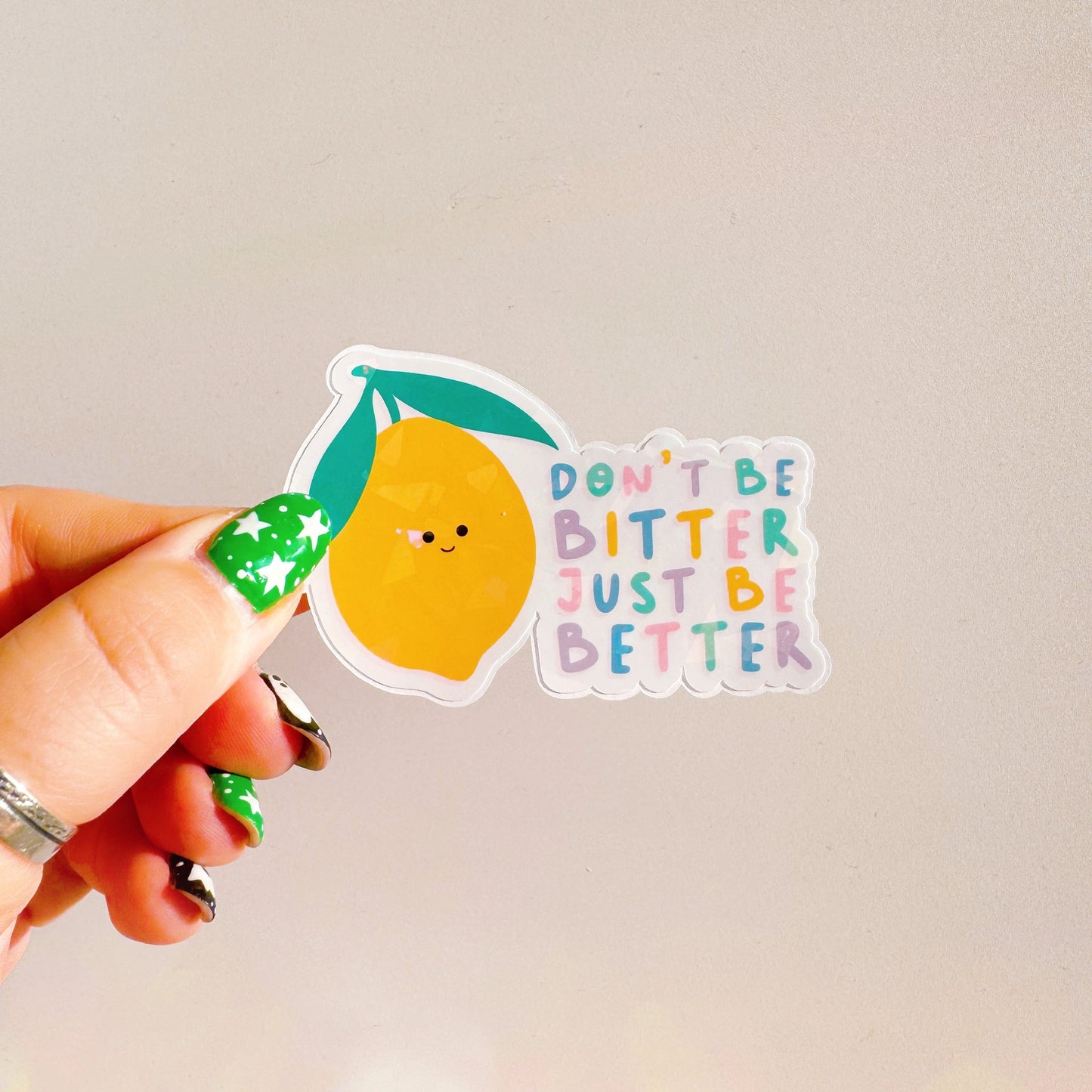 A holographic sticker, of a smiling lemon and the quote don't be bitter just be better. The sticker has an easy peel lip.