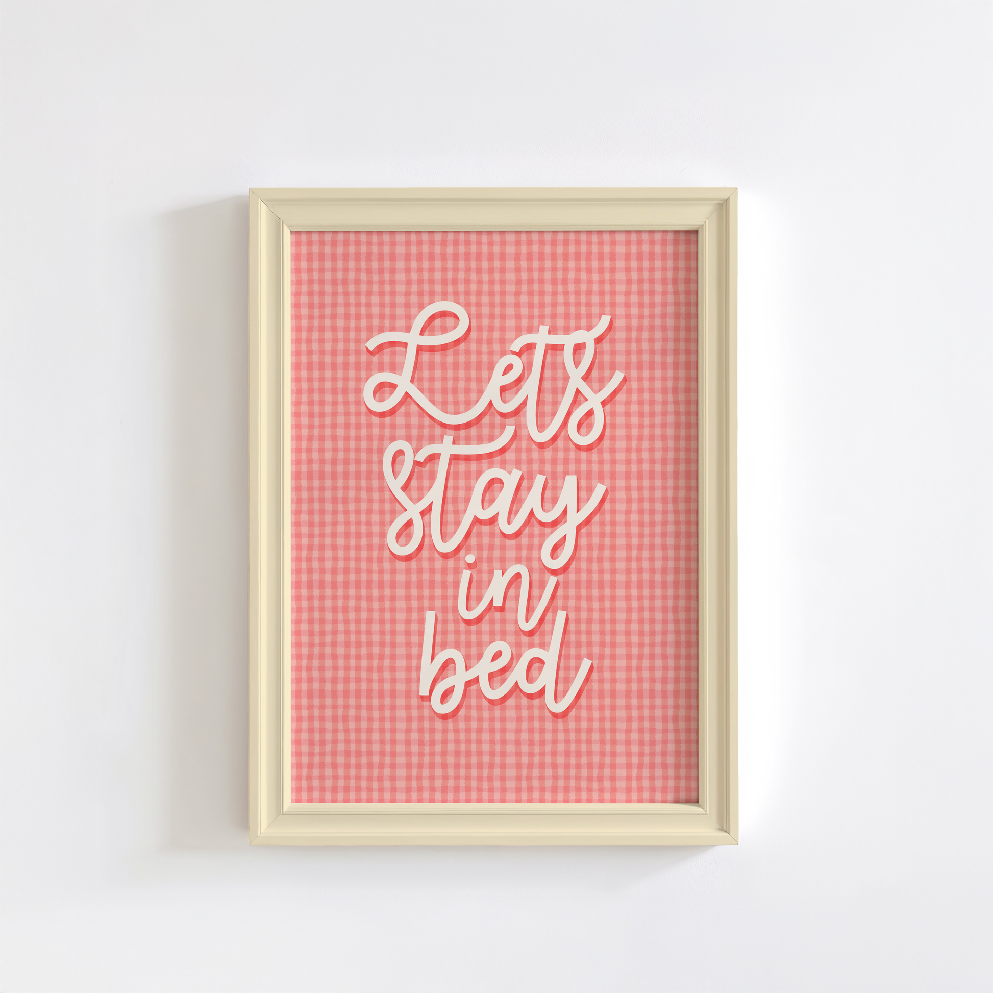 A pinky orange gingham print, with cursive handwriting that reads 'lets stay in bed' in cream.