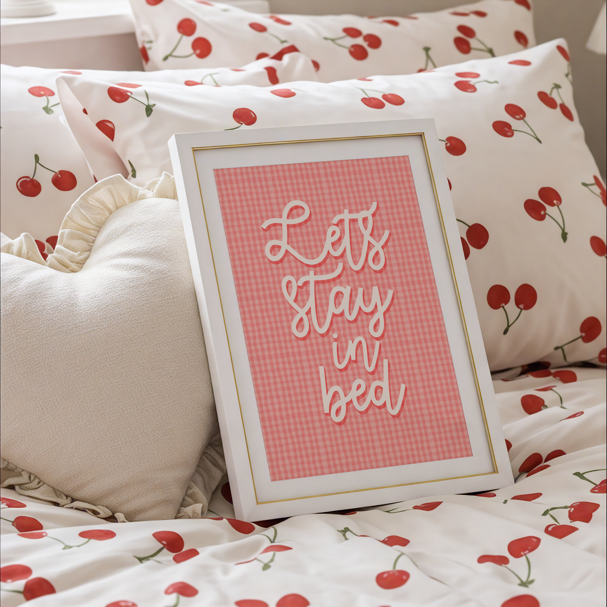 A pinky orange gingham print, with cursive handwriting that reads 'lets stay in bed' in cream.