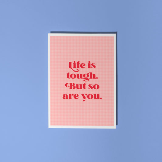 A pink and red card, that says 'life is tough but so are you.' on the front.