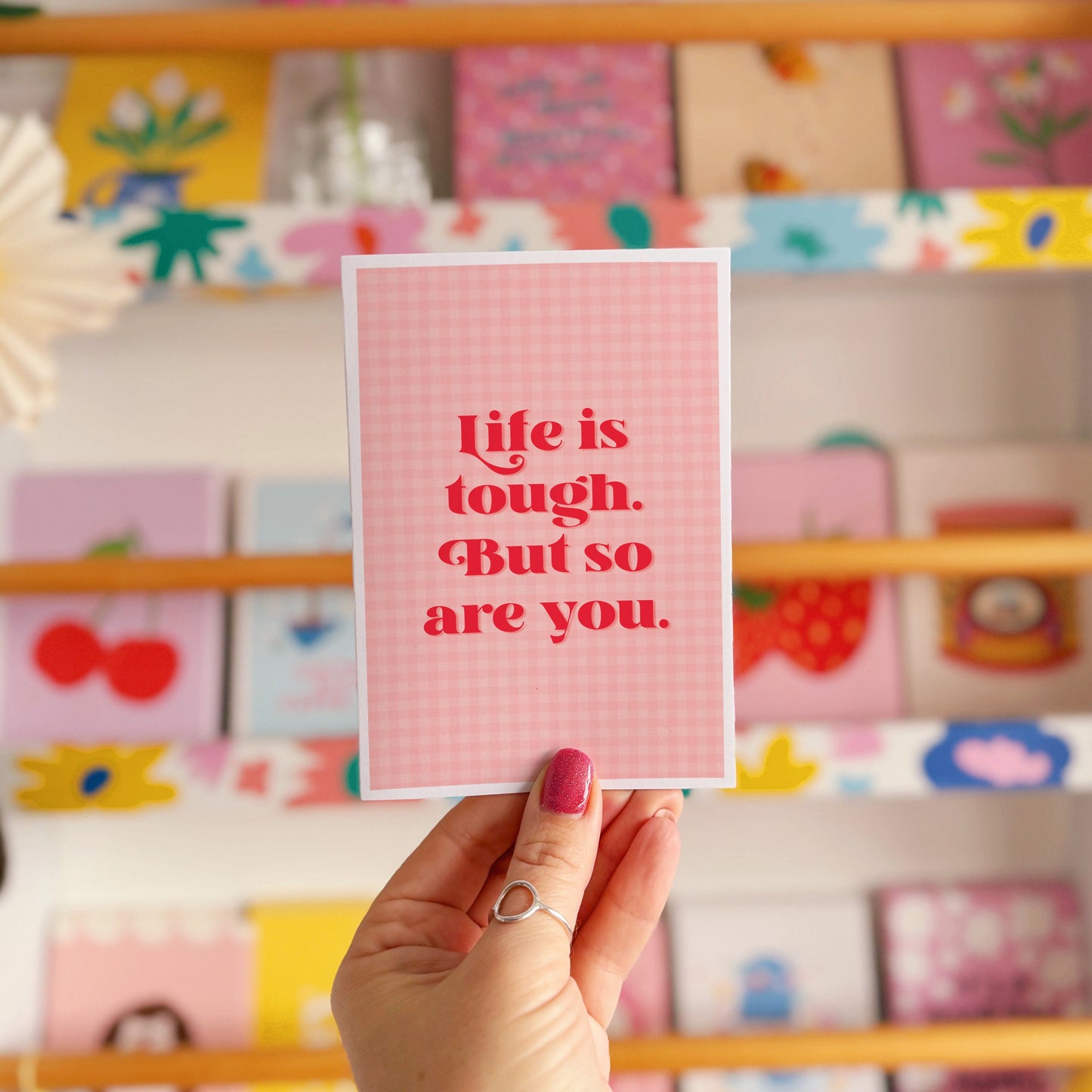 A pink and red card, that says 'life is tough but so are you.' on the front.
