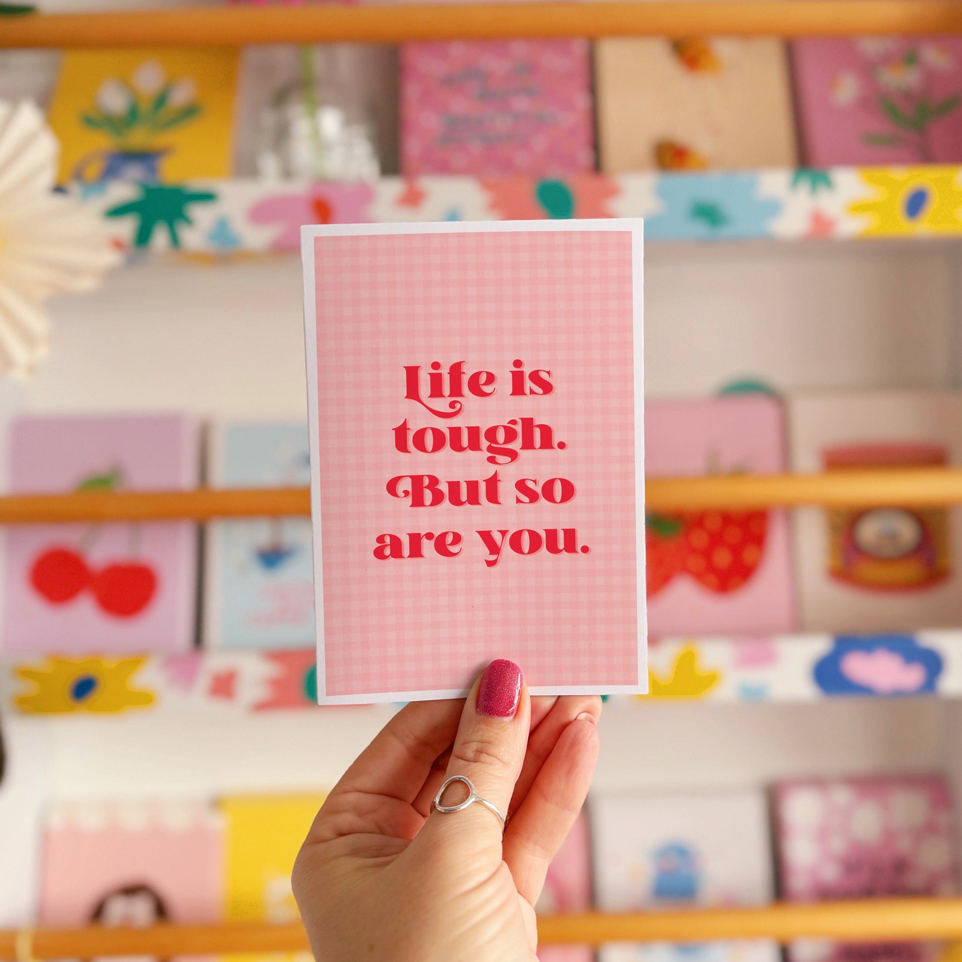 A pink and red card, that says 'life is tough but so are you.' on the front.