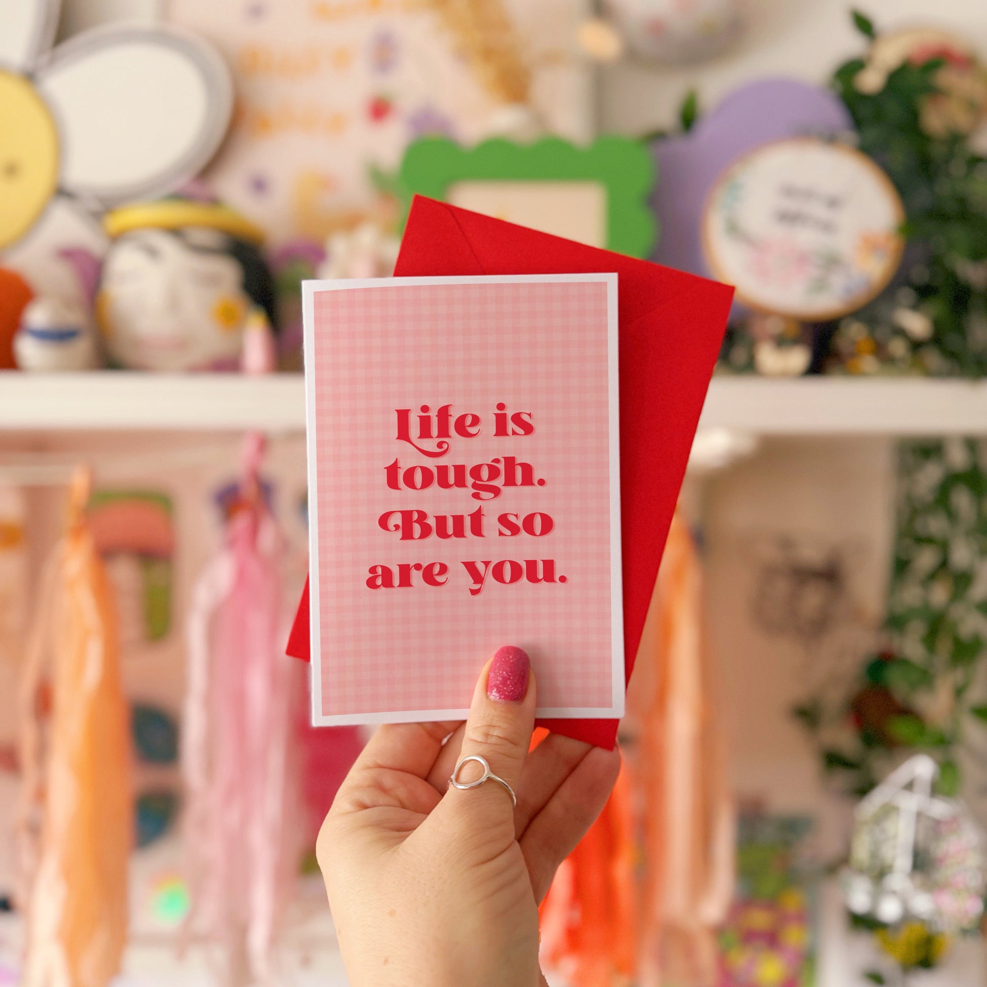 A pink and red card, that says 'life is tough but so are you.' on the front.