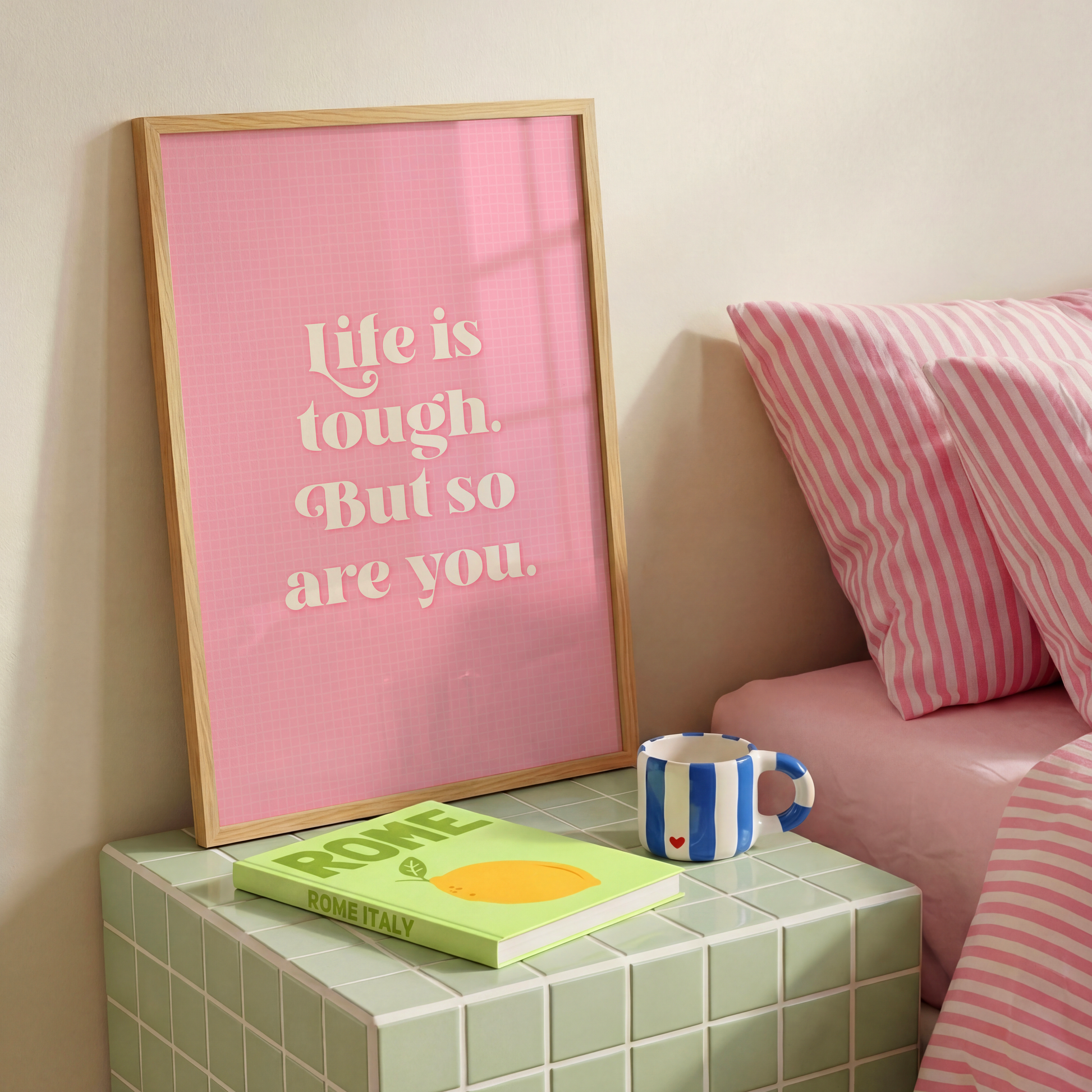 A pink print with a soft check pattern, and a quote in white that reads 'life is tough. But so are you.'.