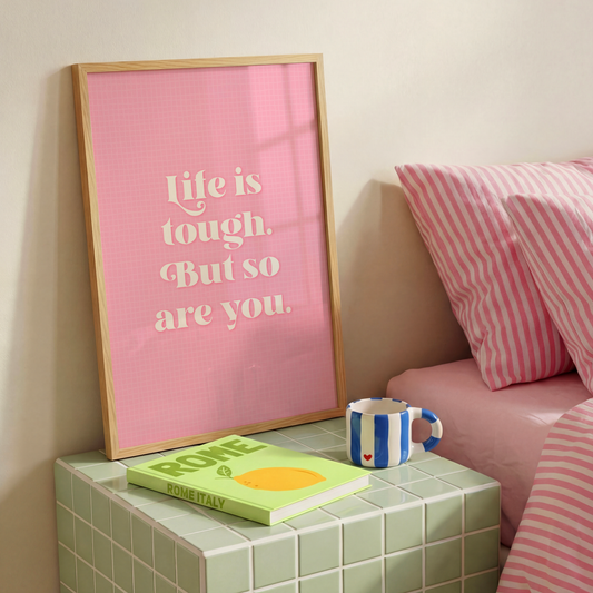 A pink print with a soft check pattern, and a quote in white that reads 'life is tough. But so are you.'.