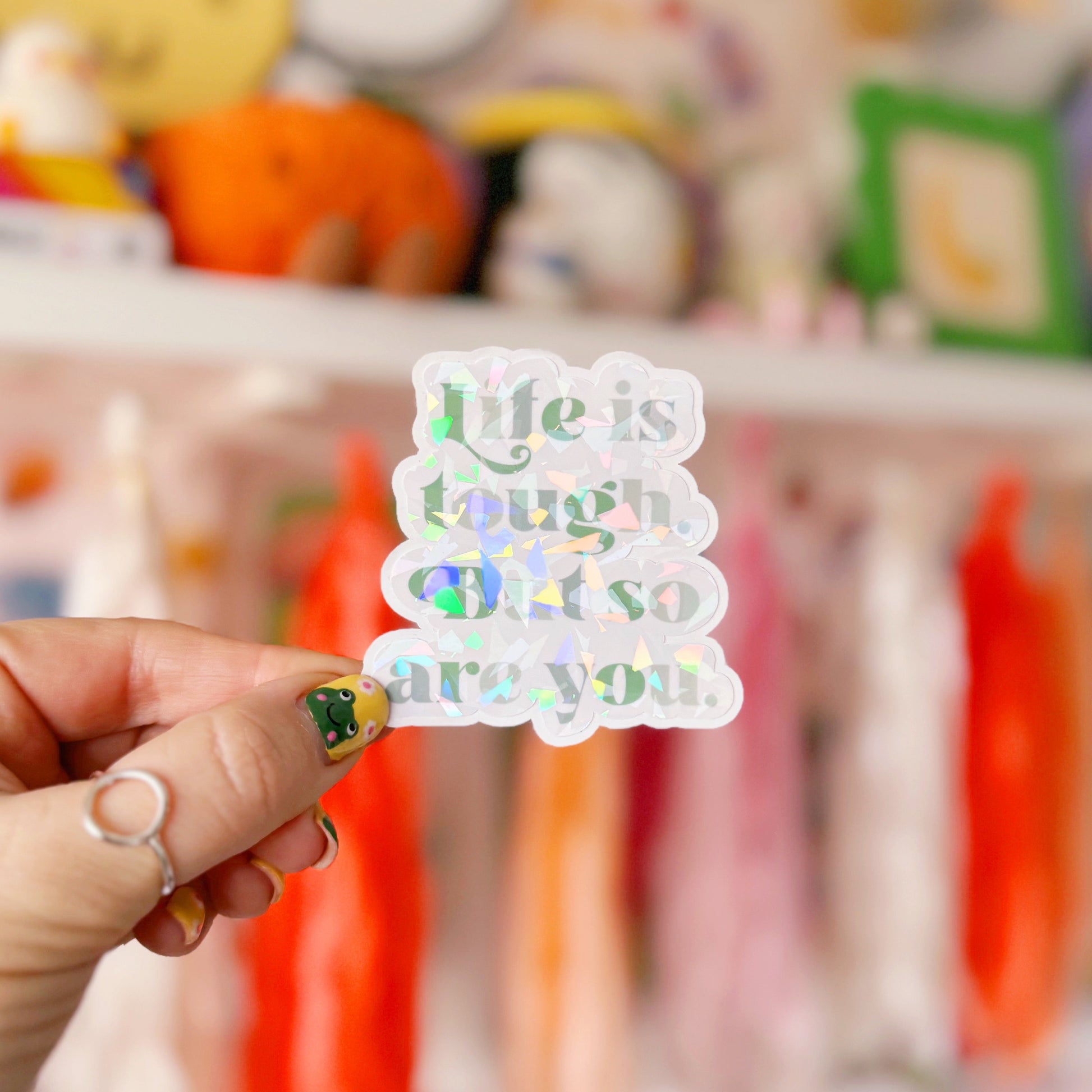 A green holographic finish sticker, with green text saying 'life is tough but so are you'.