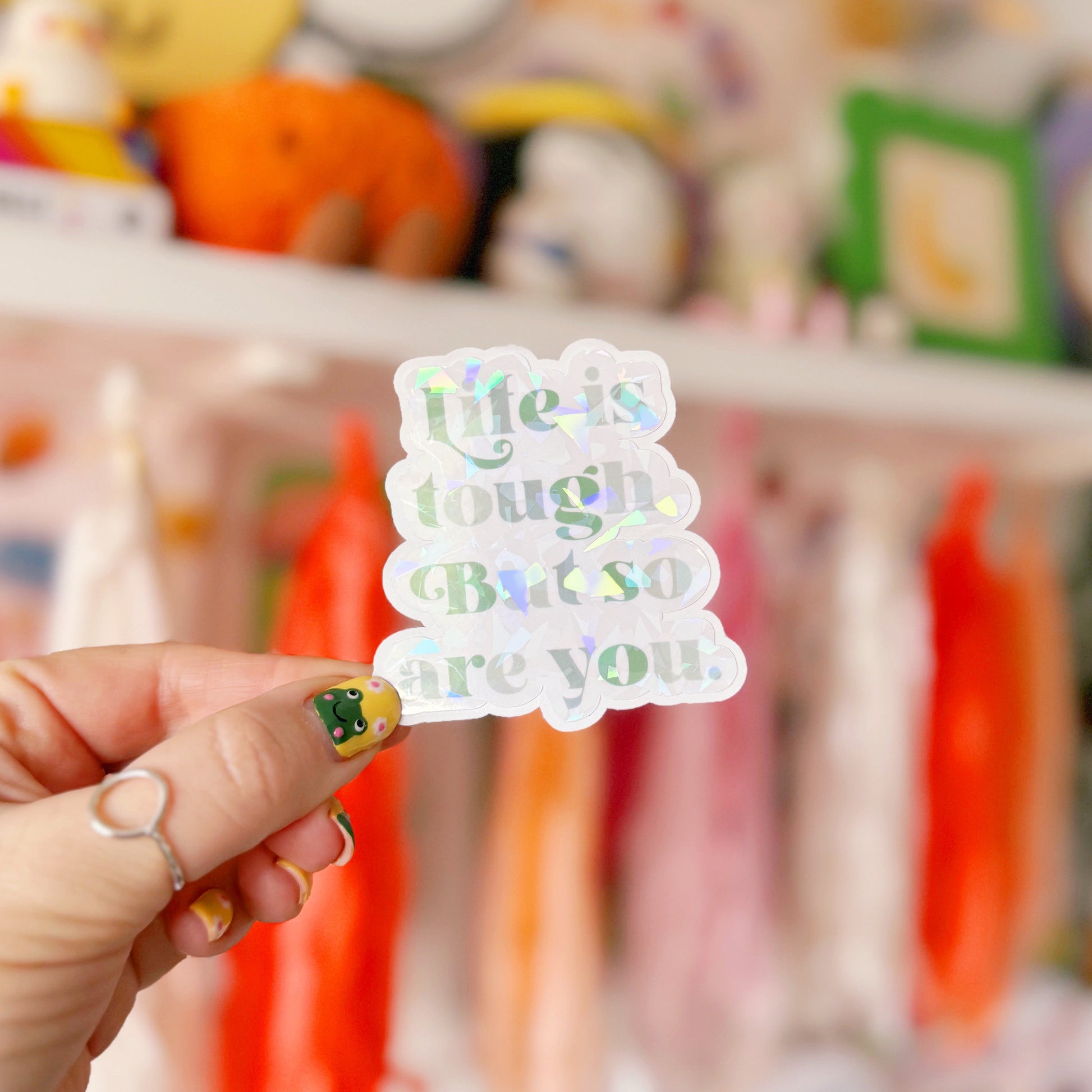 A green holographic finish sticker, with green text saying 'life is tough but so are you'.