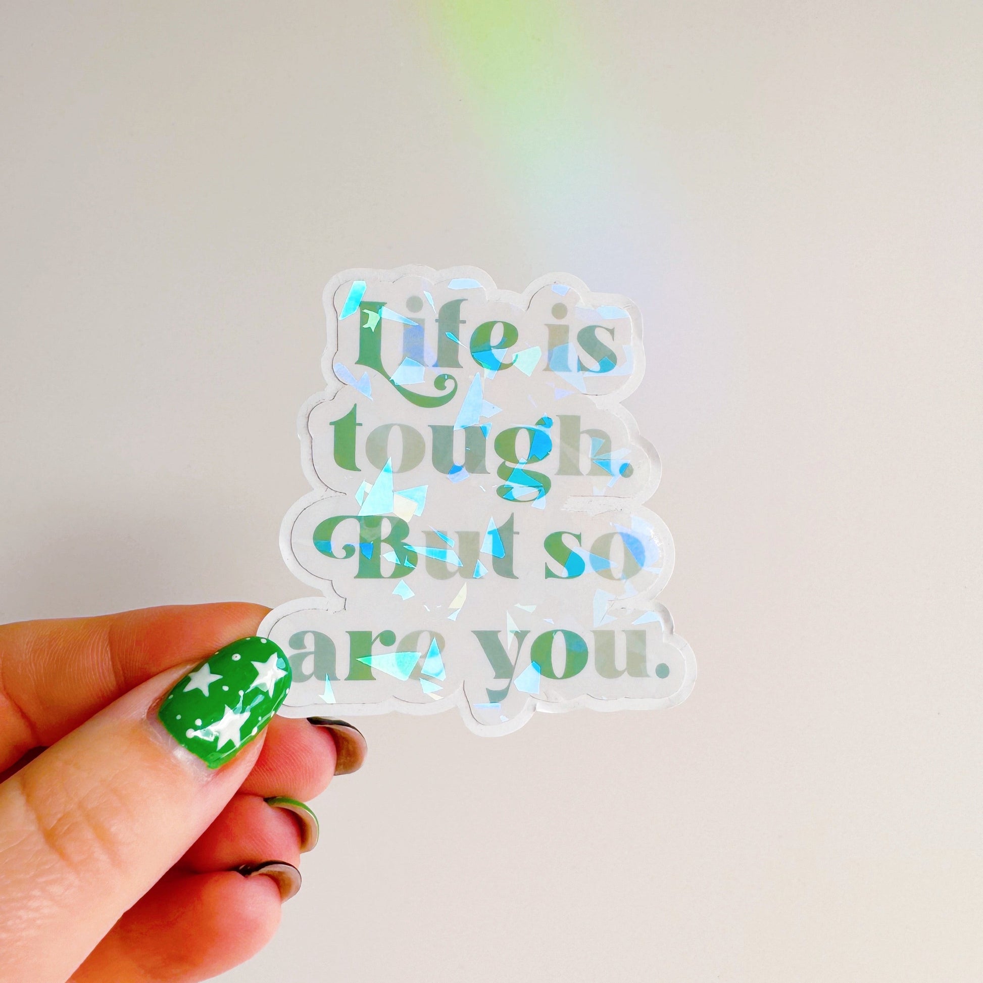 A holographic sticker, saying life is tough but so are you. The sticker has an easy peel lip.