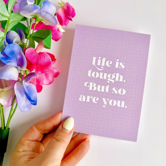 A textured postcard, with the words life is tough but so are you, on the front, on a purple background.