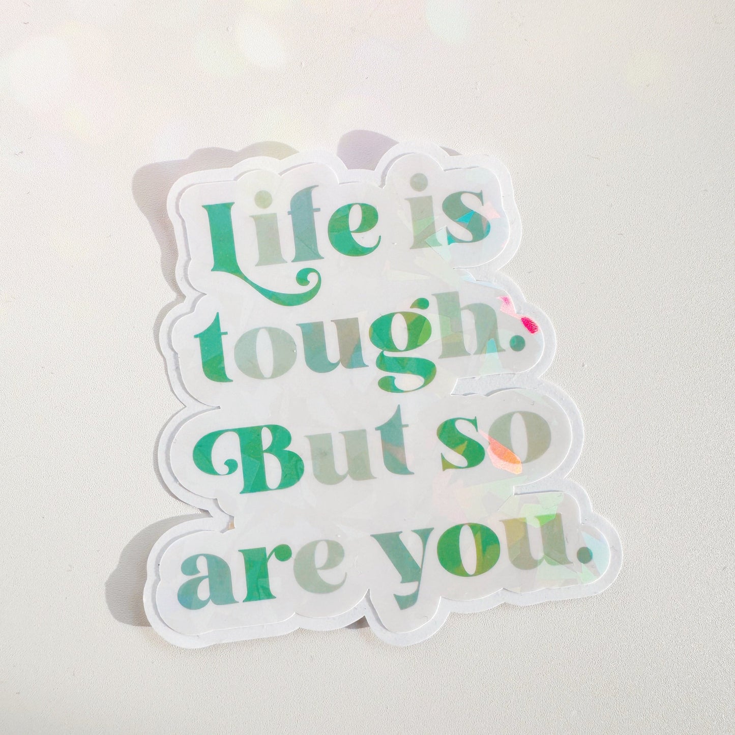 A holographic sticker, saying life is tough but so are you. The sticker has an easy peel lip.