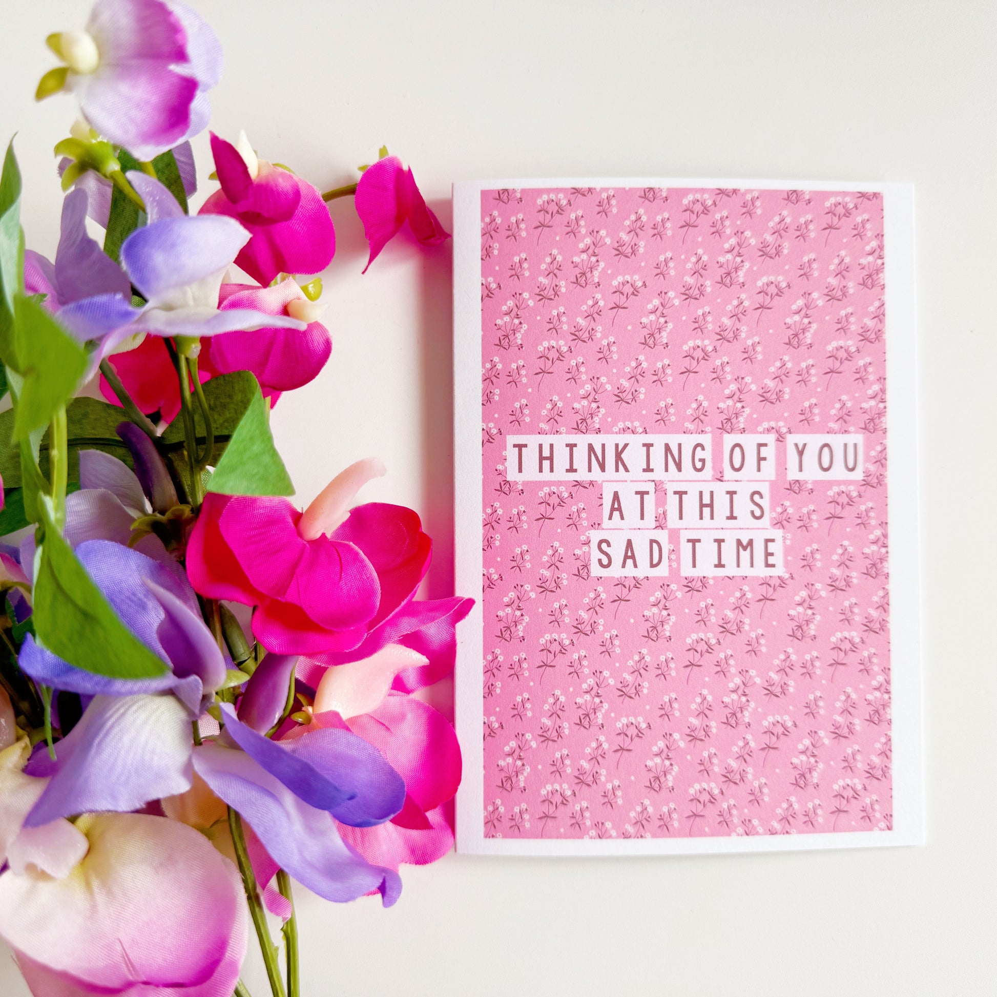 A card with a pink floral patterned background, and the words 'thinking of you at this sad time' in the centre.