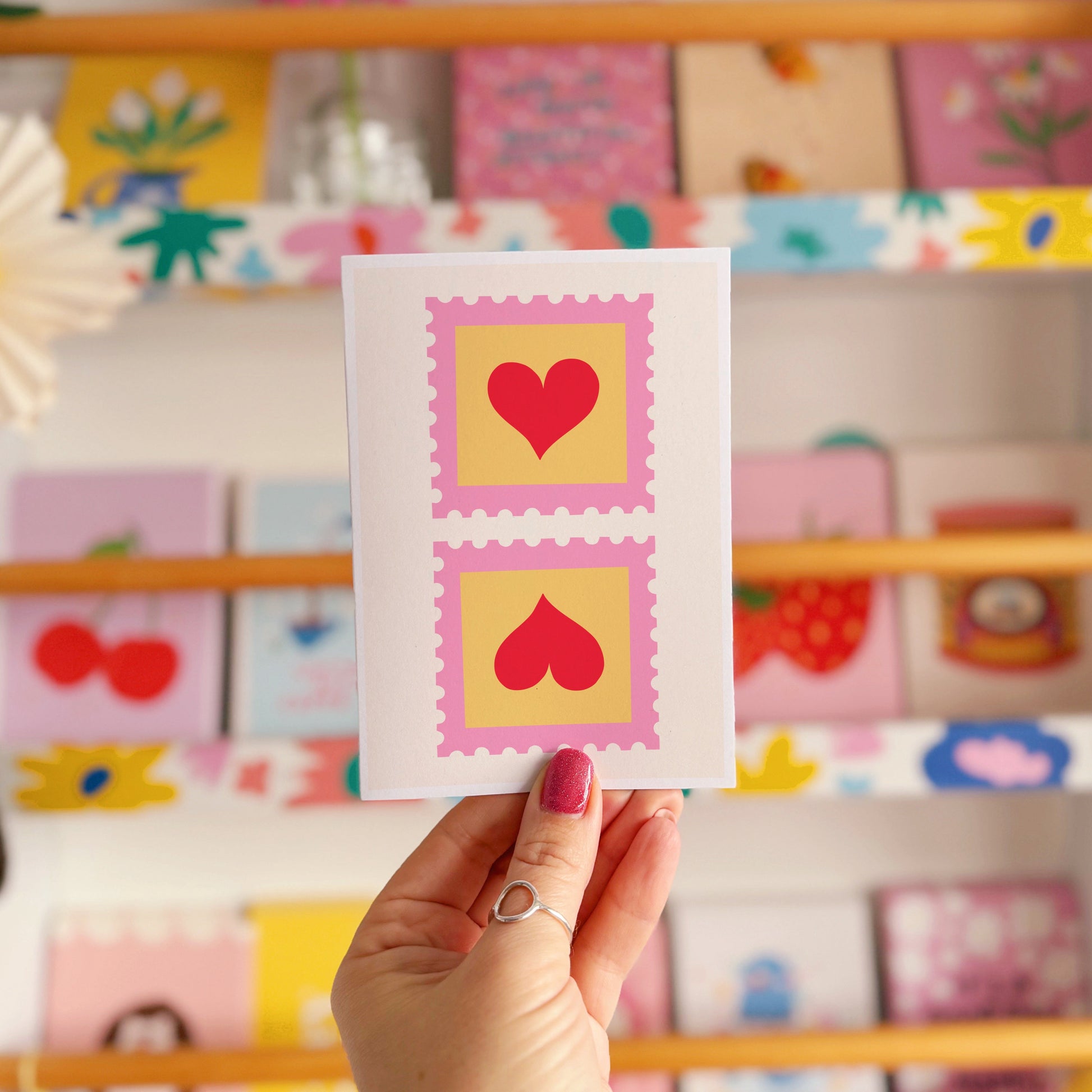 An illustrated card with two love heart postage stamps on the front, in pink, yellow and red.