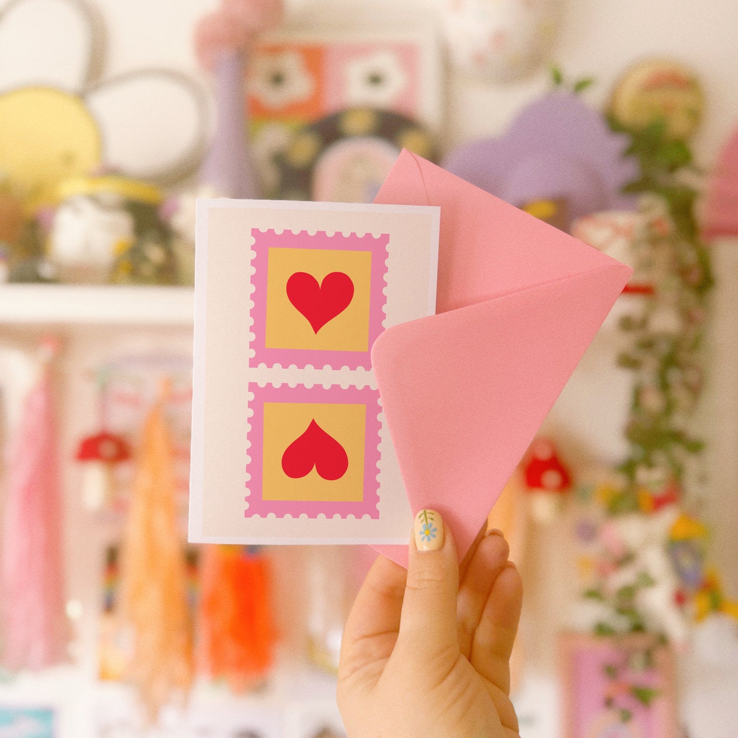 An illustrated card with two love heart postage stamps on the front, in pink, yellow and red.