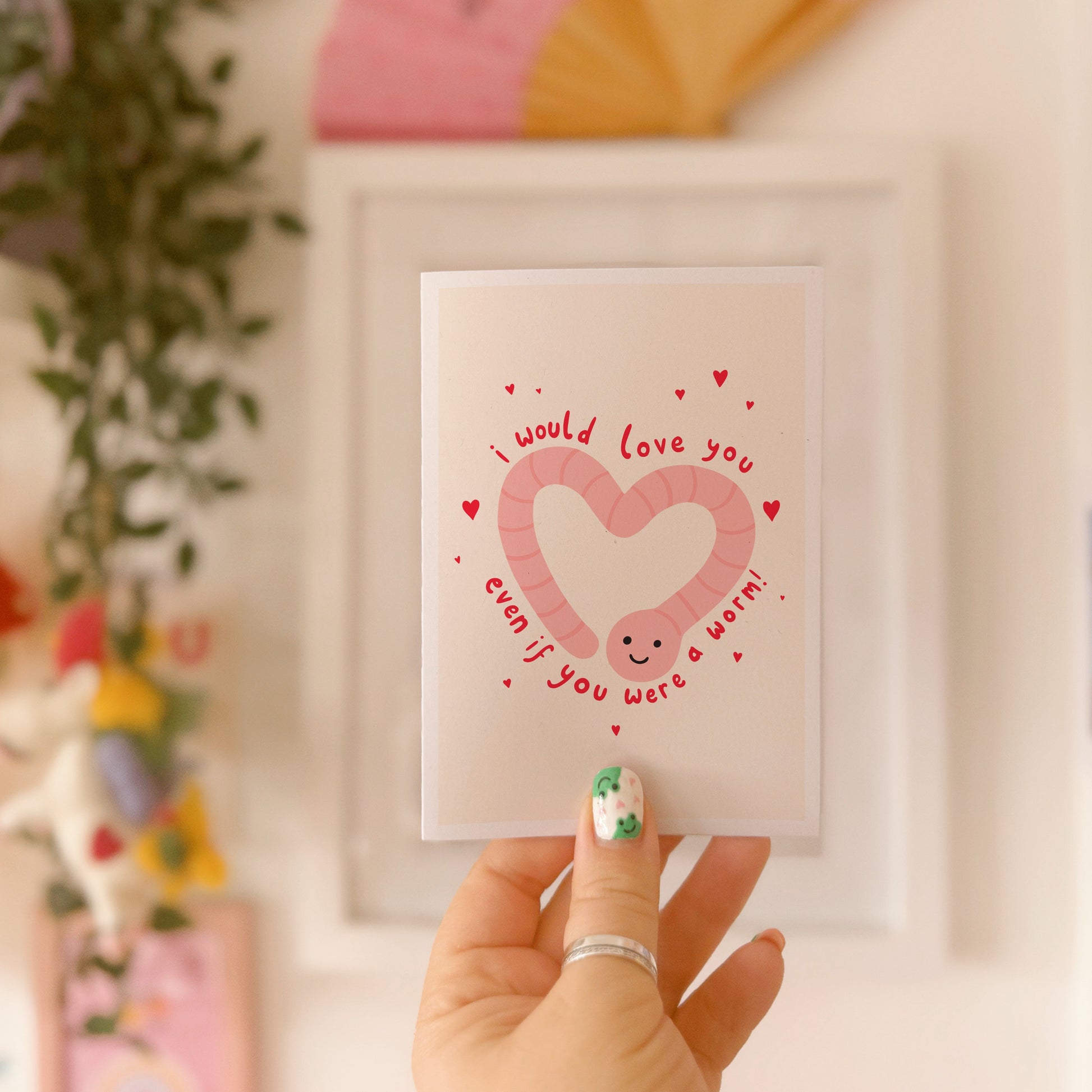 An illustrated card with a drawing of a cute smiling worm on the front, in the shape of a heart. Around the worm is text that reads 'I would love you even if you were a worm!'.