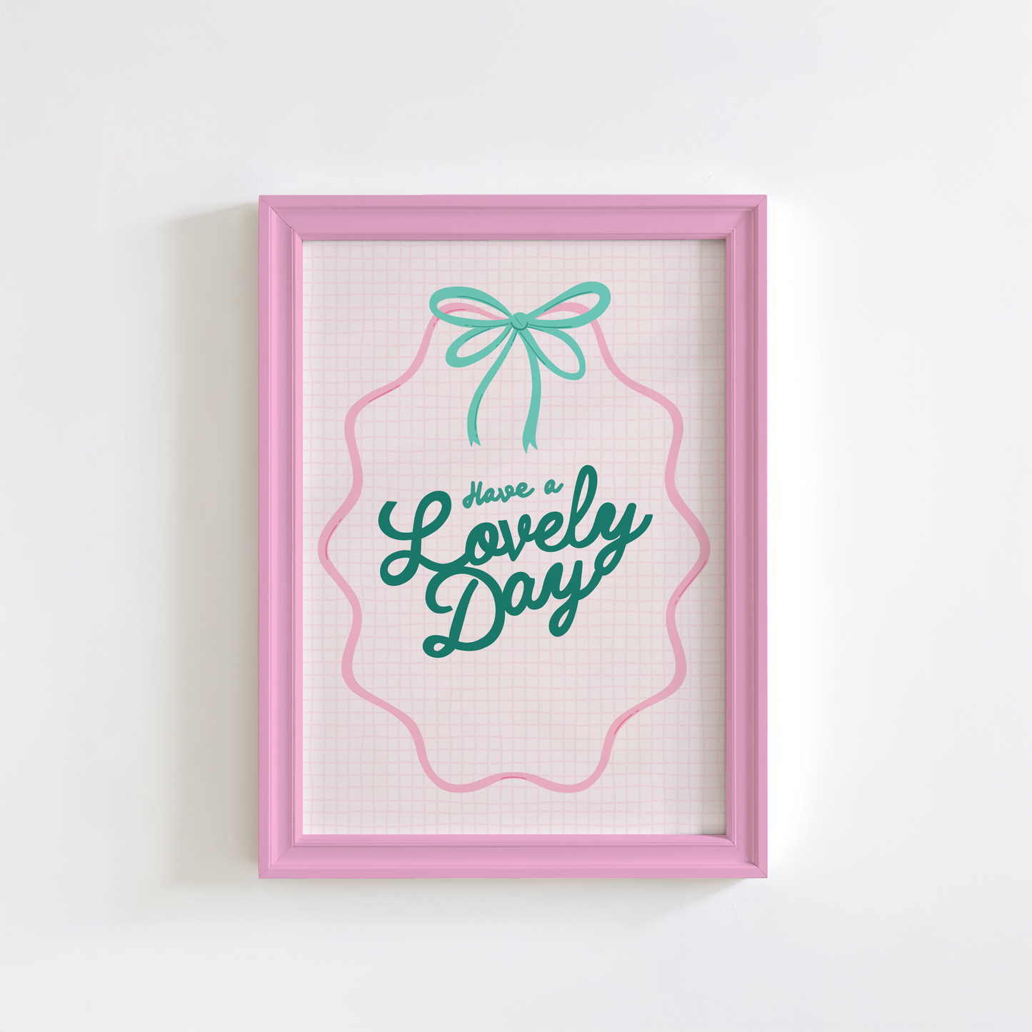 A print with a soft pink check background, and the words 'Have a lovely day' in teal handwriting in the centre. The words are framed by a pink ribbon with a teal bow at the top.