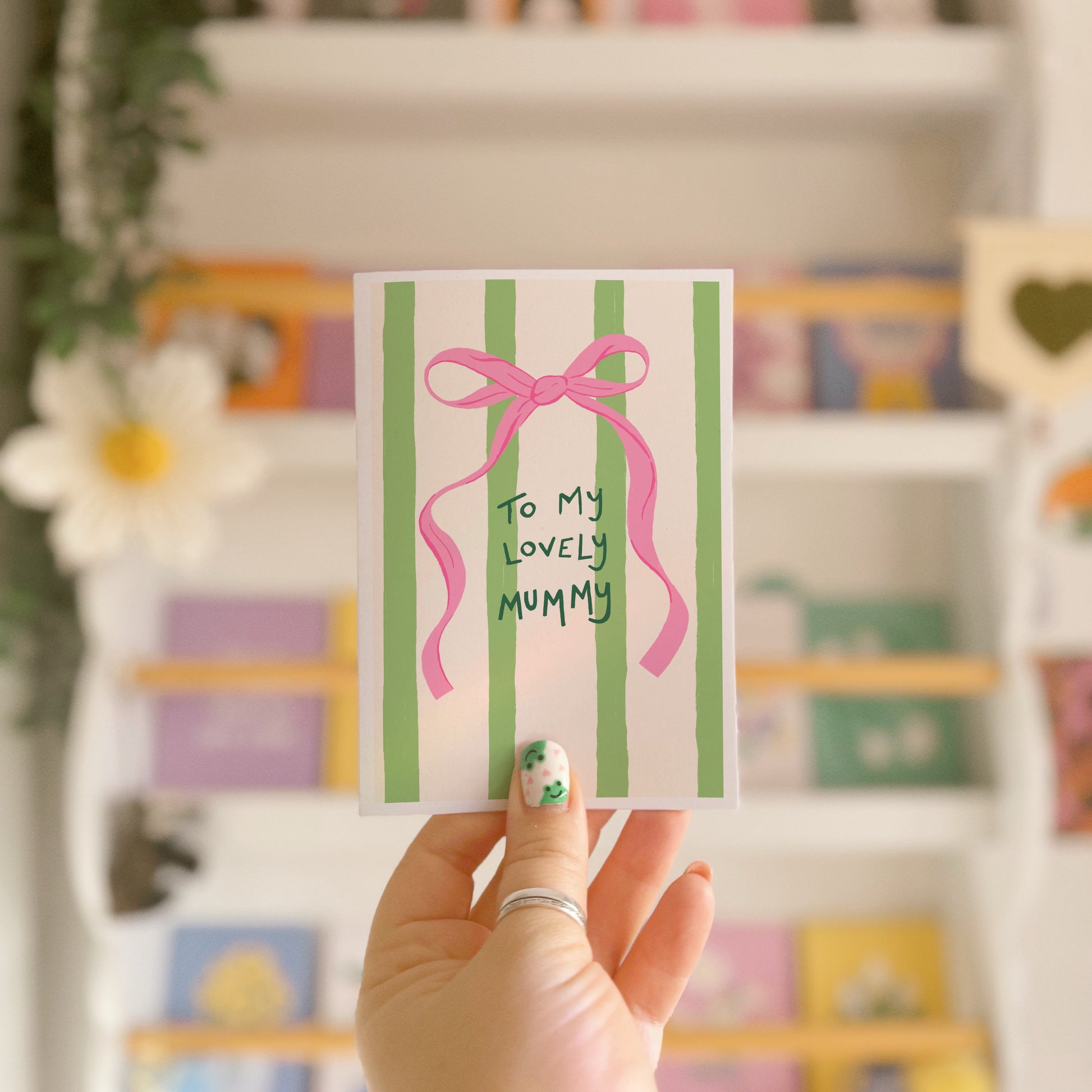 A cream and green striped card, with a pink bow, and handwritten text that says 'to my lovely mummy'.