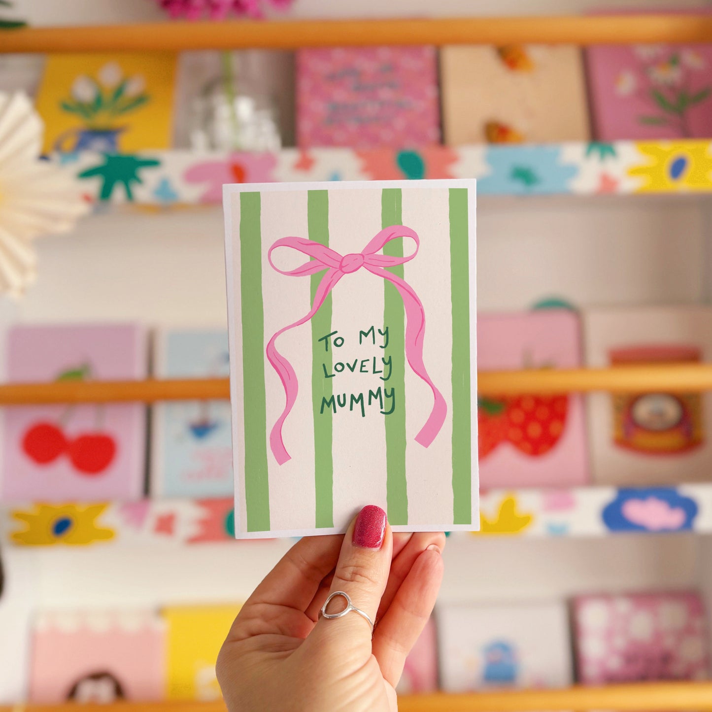 A cream and green striped card, with a pink bow, and handwritten text that says 'to my lovely mummy'.